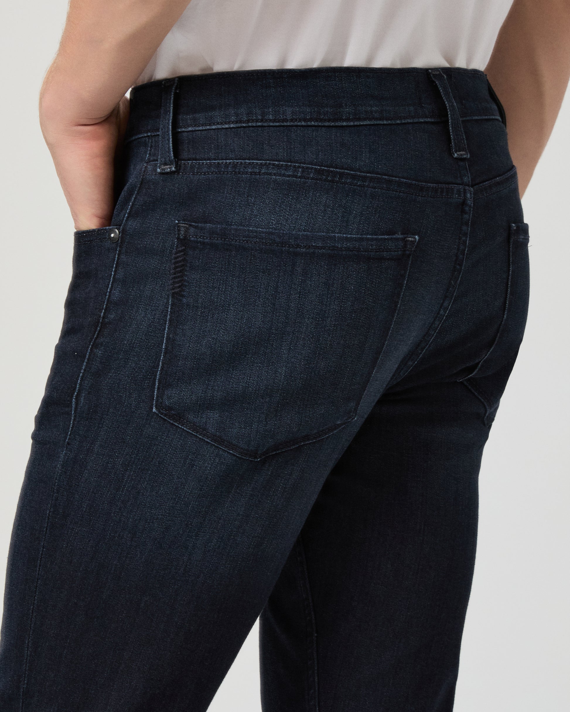 Person wearing dark blue jeans and white shoes on a light gray background