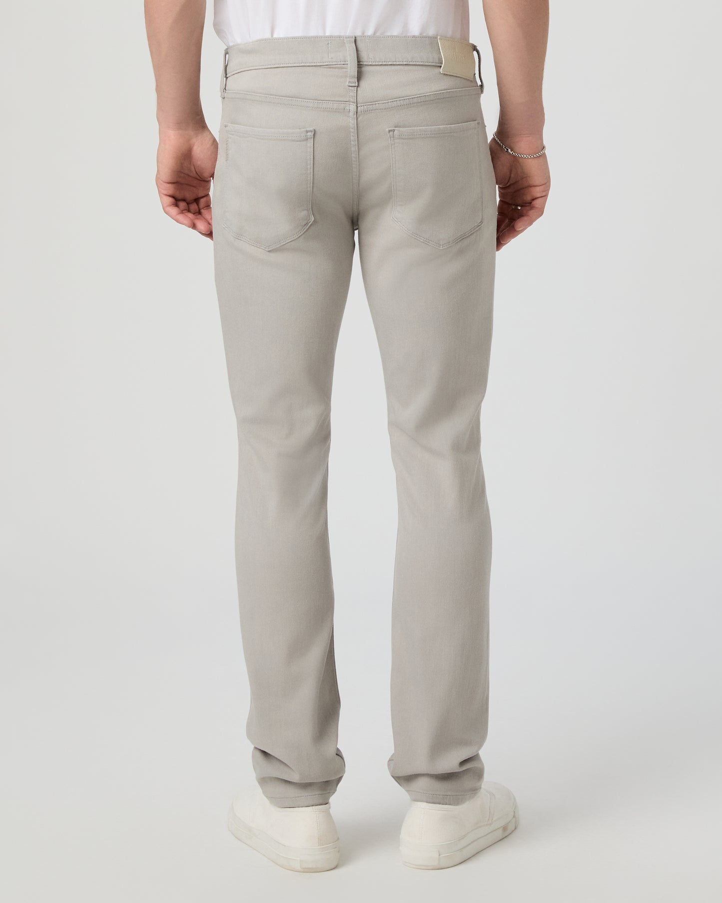 Man wearing a white shirt and grey jeans on a light gray background