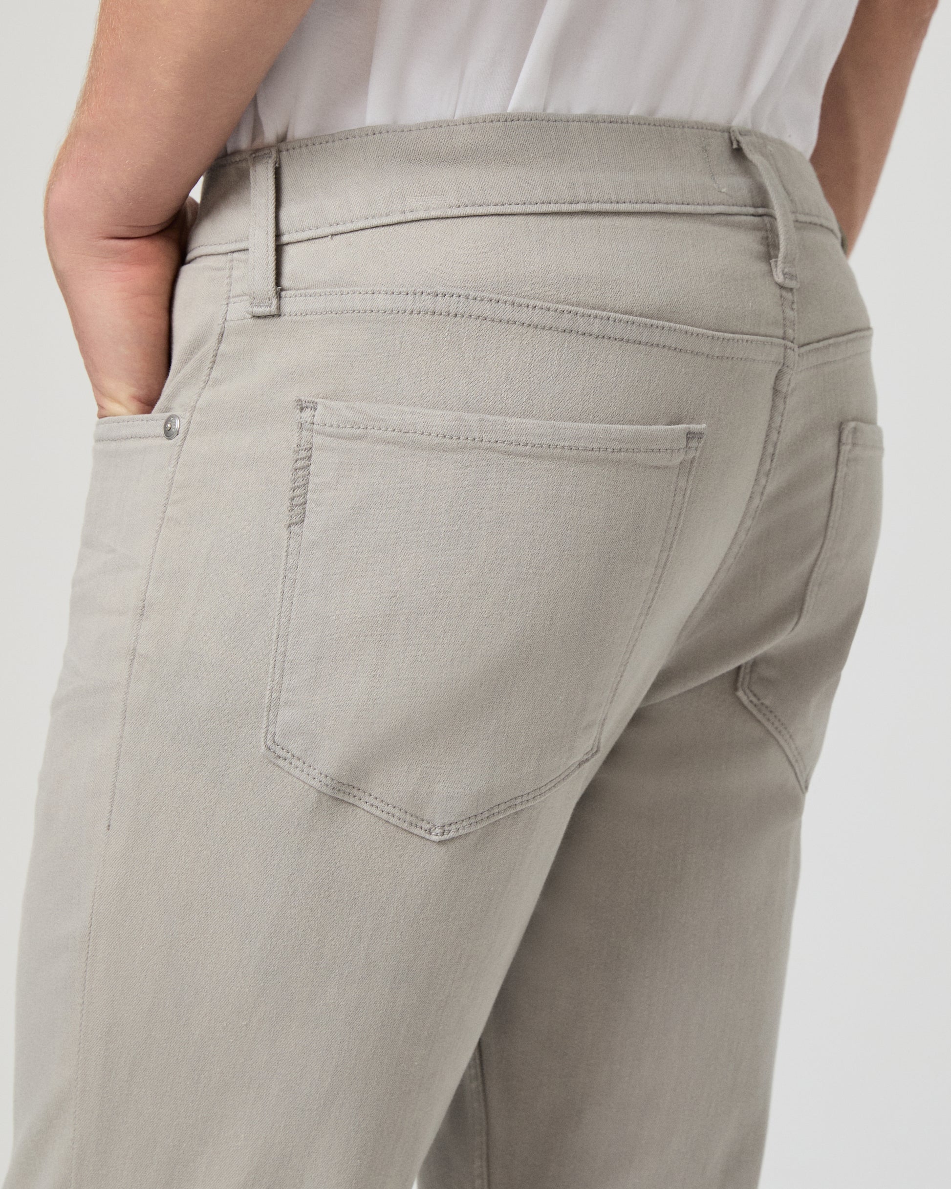 Man wearing a white shirt and grey jeans on a light gray background
