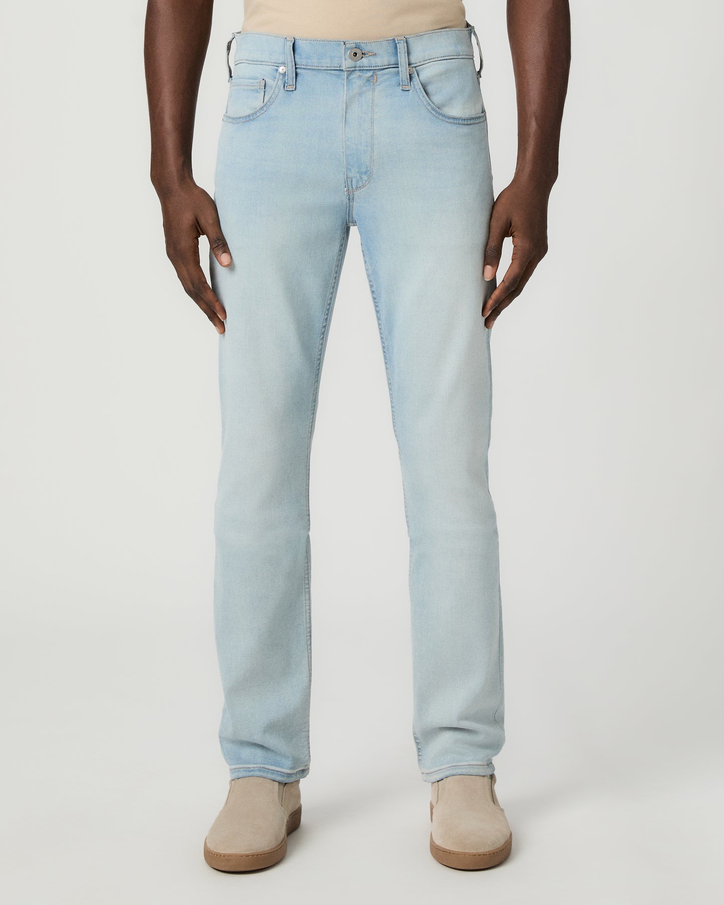 Man wearing beige tee, light blue jeans, and brown shoes on a white background