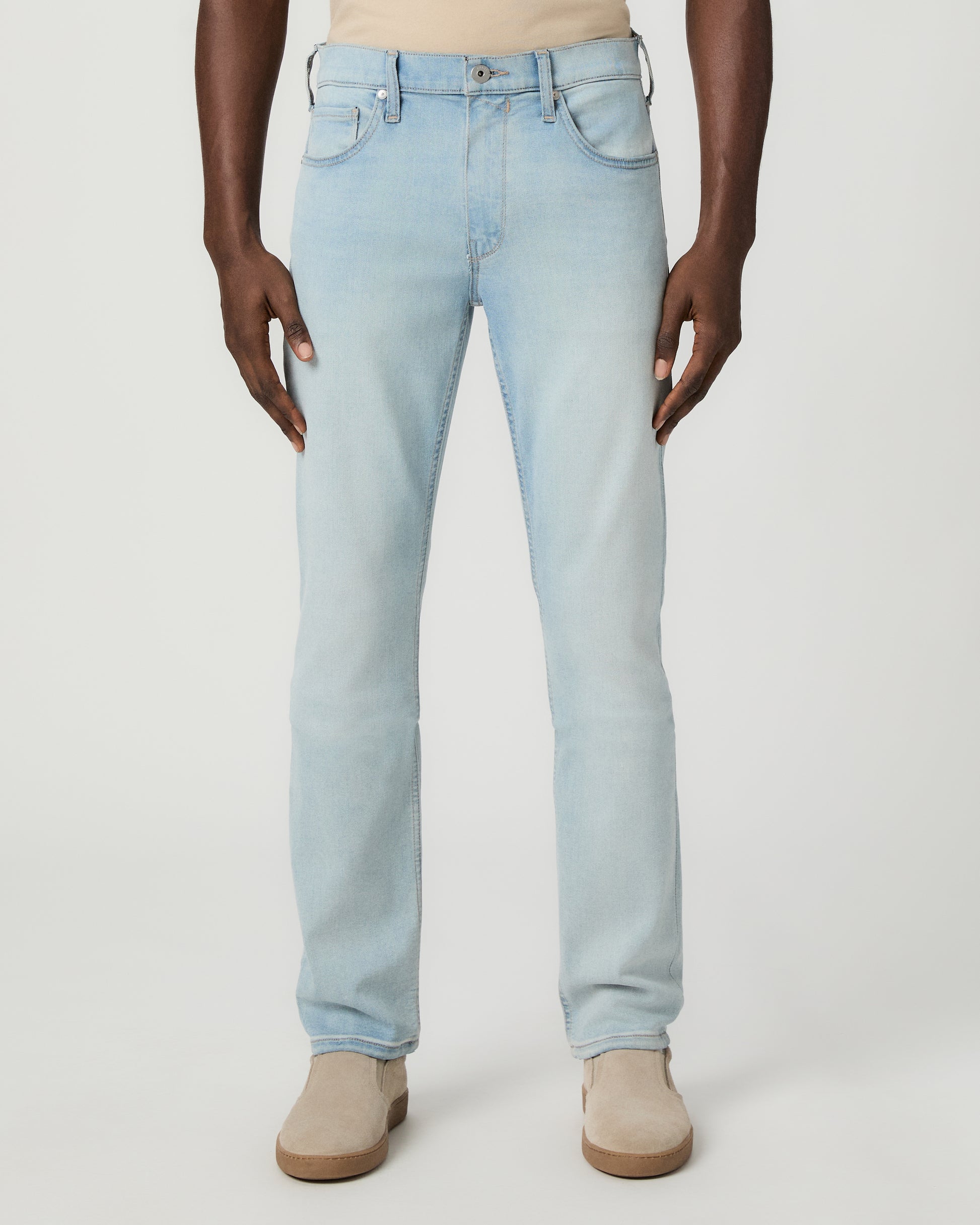 Man wearing beige tee, light blue jeans, and brown shoes on a white background
