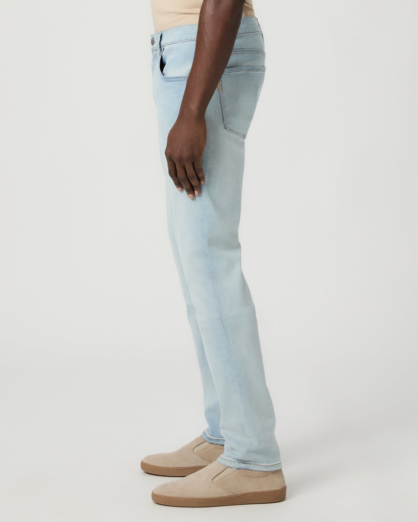 Man wearing beige tee, light blue jeans, and brown shoes on a white background