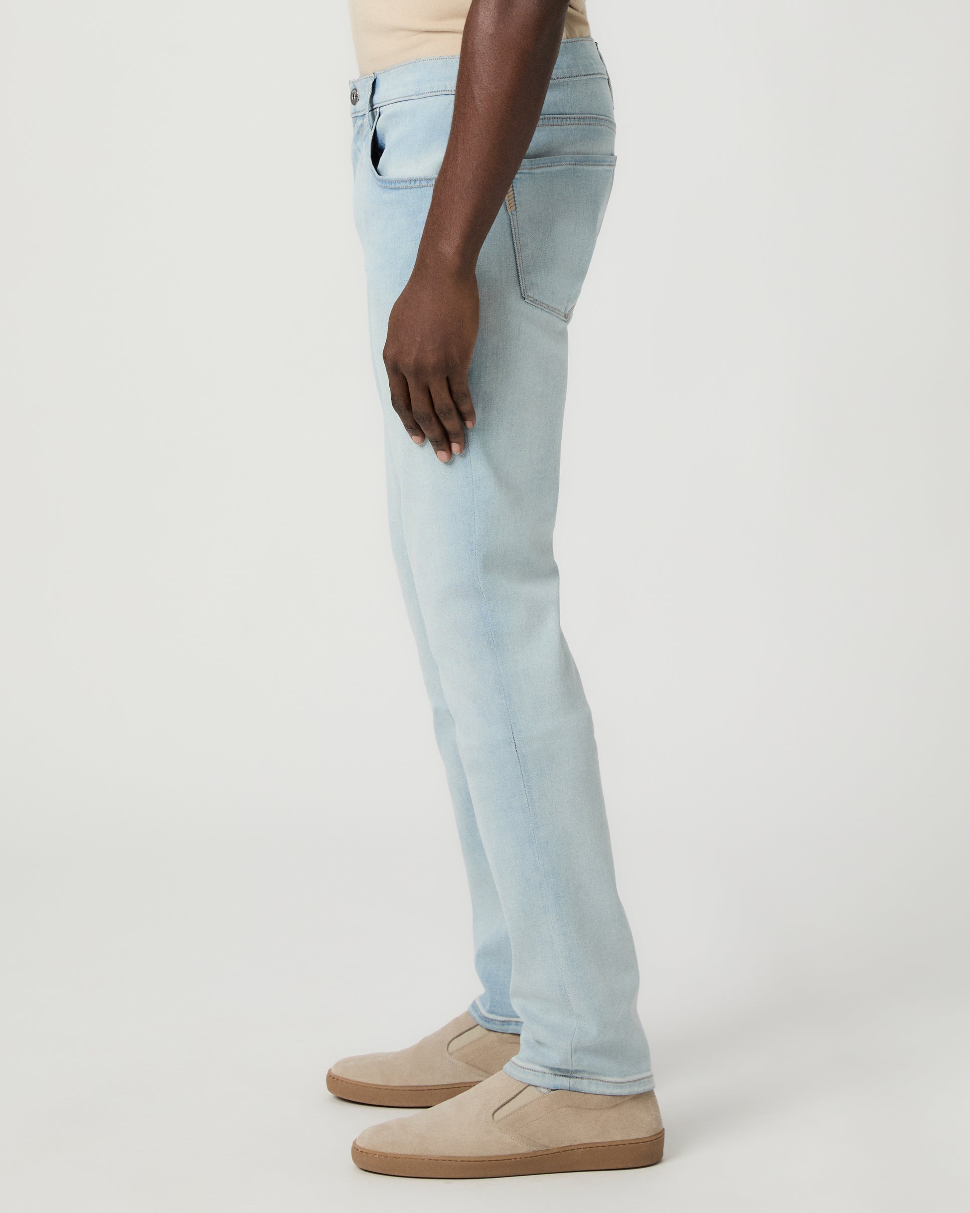 Man wearing beige tee, light blue jeans, and brown shoes on a white background