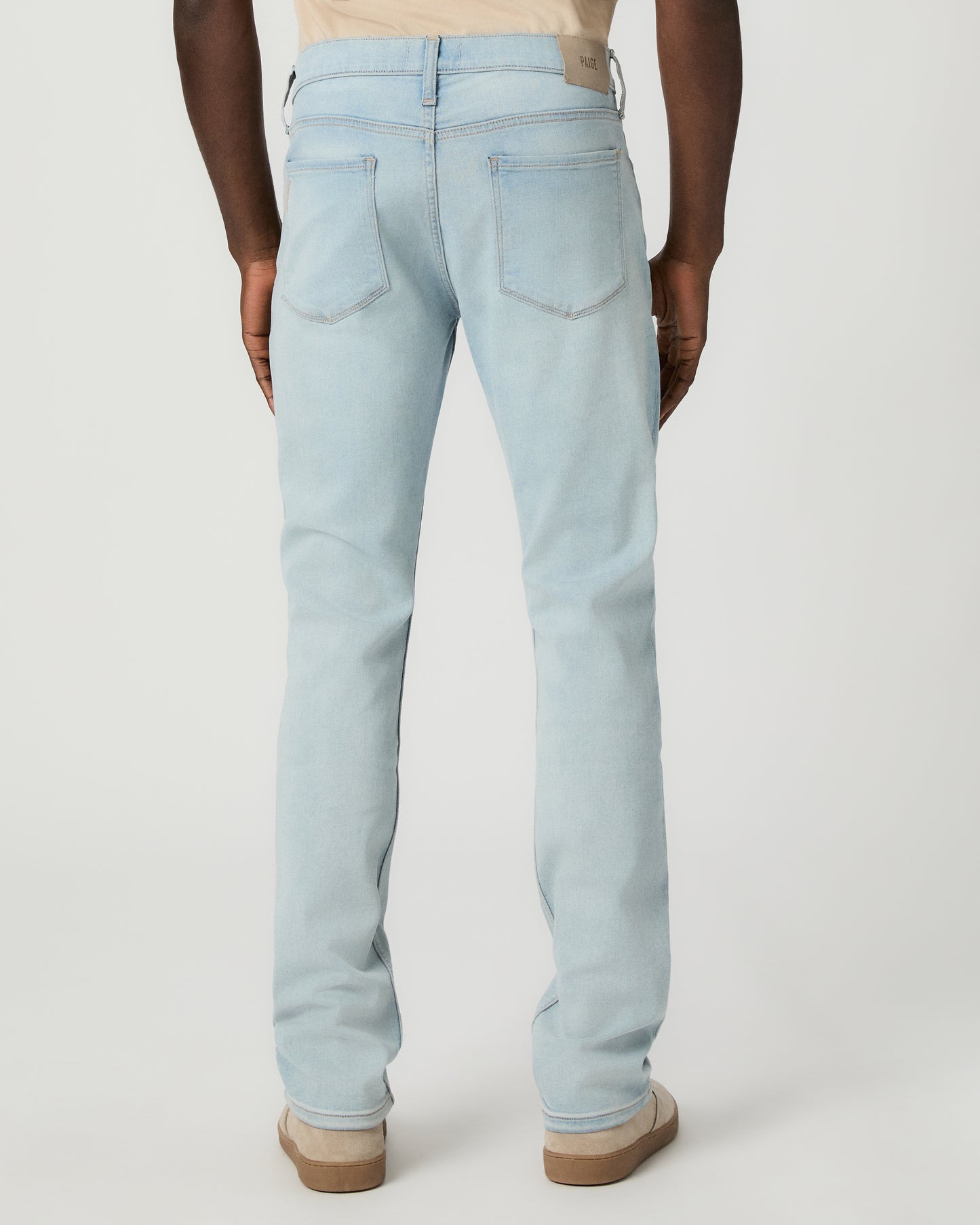 Man wearing beige tee, light blue jeans, and brown shoes on a white background