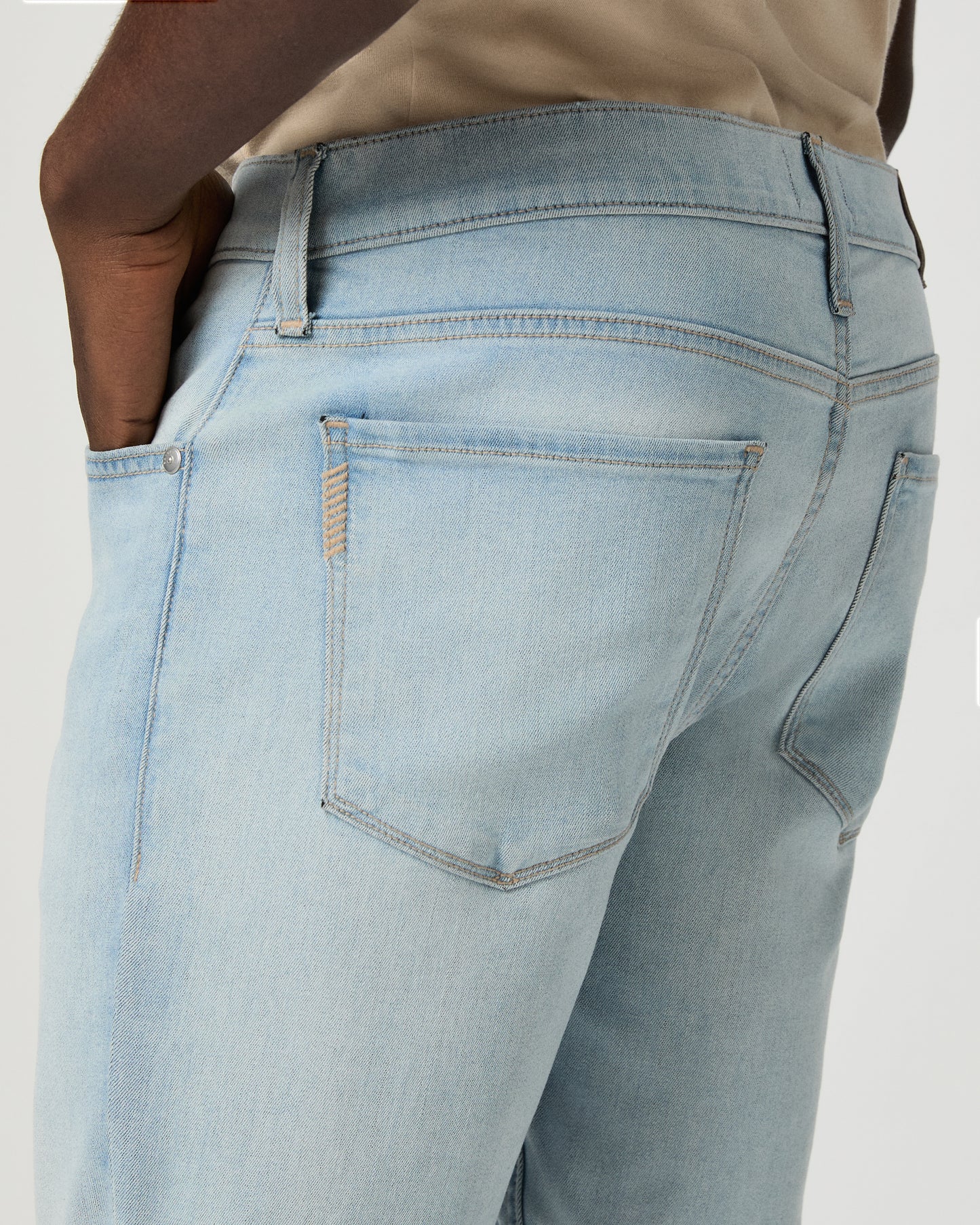 Man wearing beige tee, light blue jeans, and brown shoes on a white background