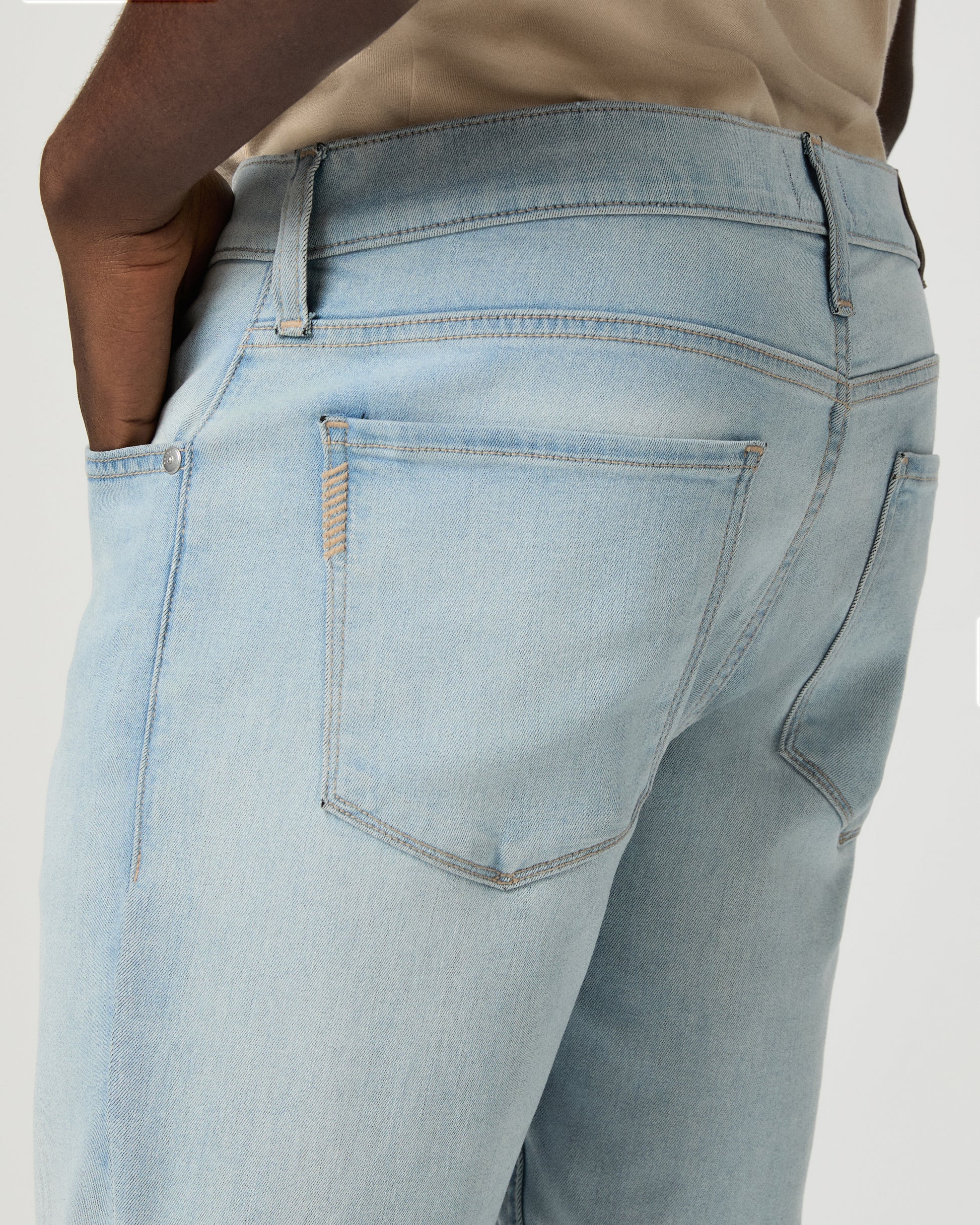 Man wearing beige tee, light blue jeans, and brown shoes on a white background