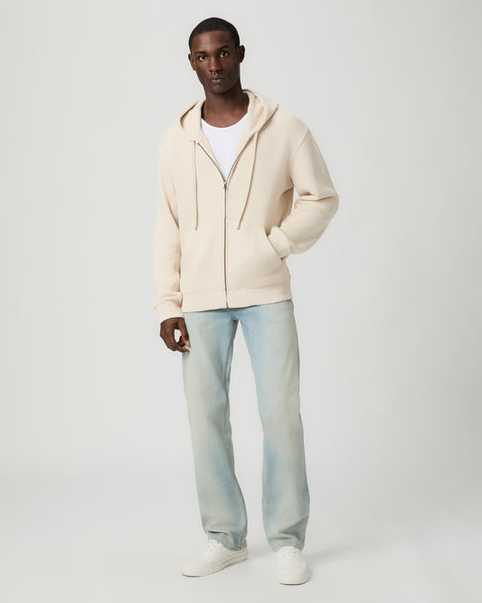 Man wearing a beige hoodie and light blue jeans on a white background