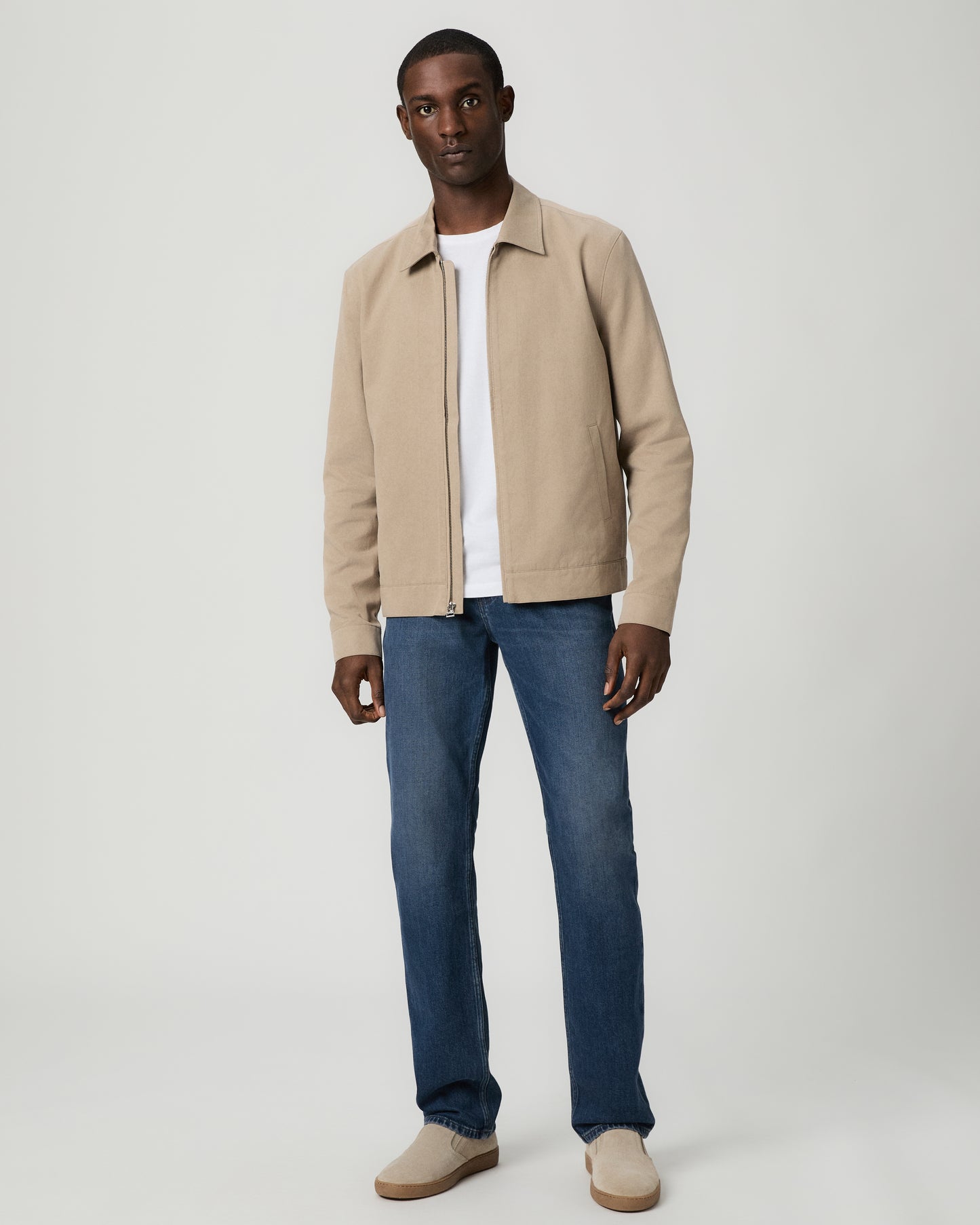 Man wearing a beige jacket, white shirt, and blue jeans on a white background