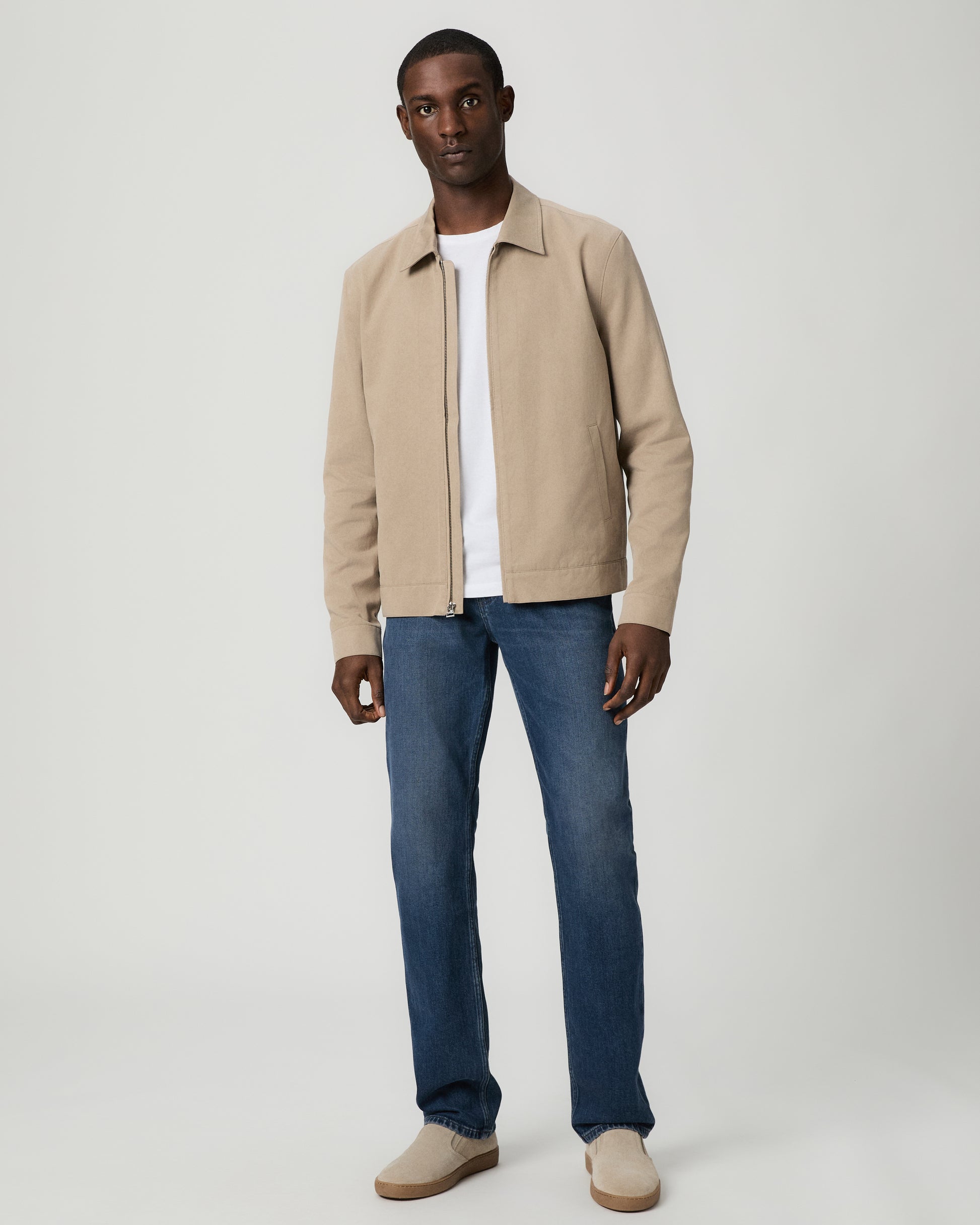 Man wearing a beige jacket, white shirt, and blue jeans on a white background