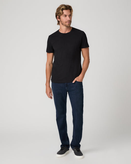 A man modeling a black short-sleeve crewneck t-shirt and dark blue jeans against a light gray studio background.