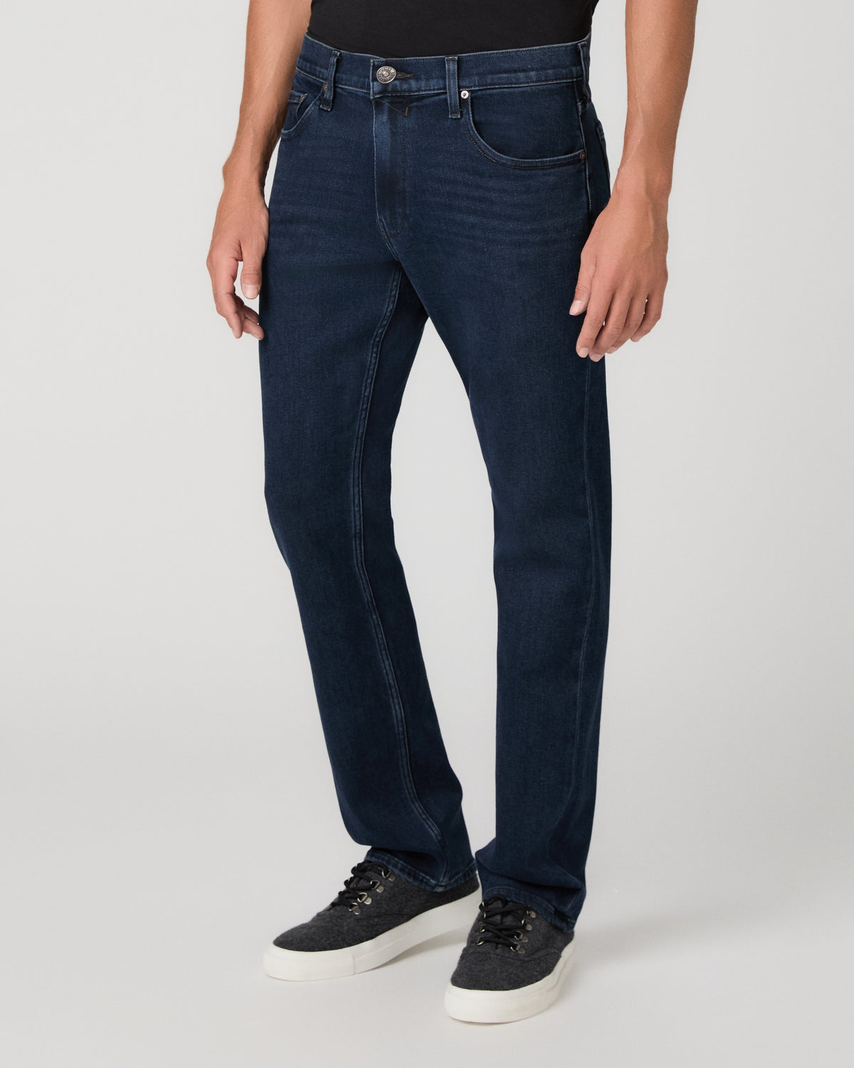 A man modeling a black short-sleeve crewneck t-shirt and dark blue jeans against a light gray studio background.
