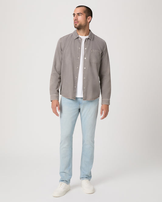 Man wearing a gray shirt over a white t-shirt, light blue jeans, and white sneakers on a white background