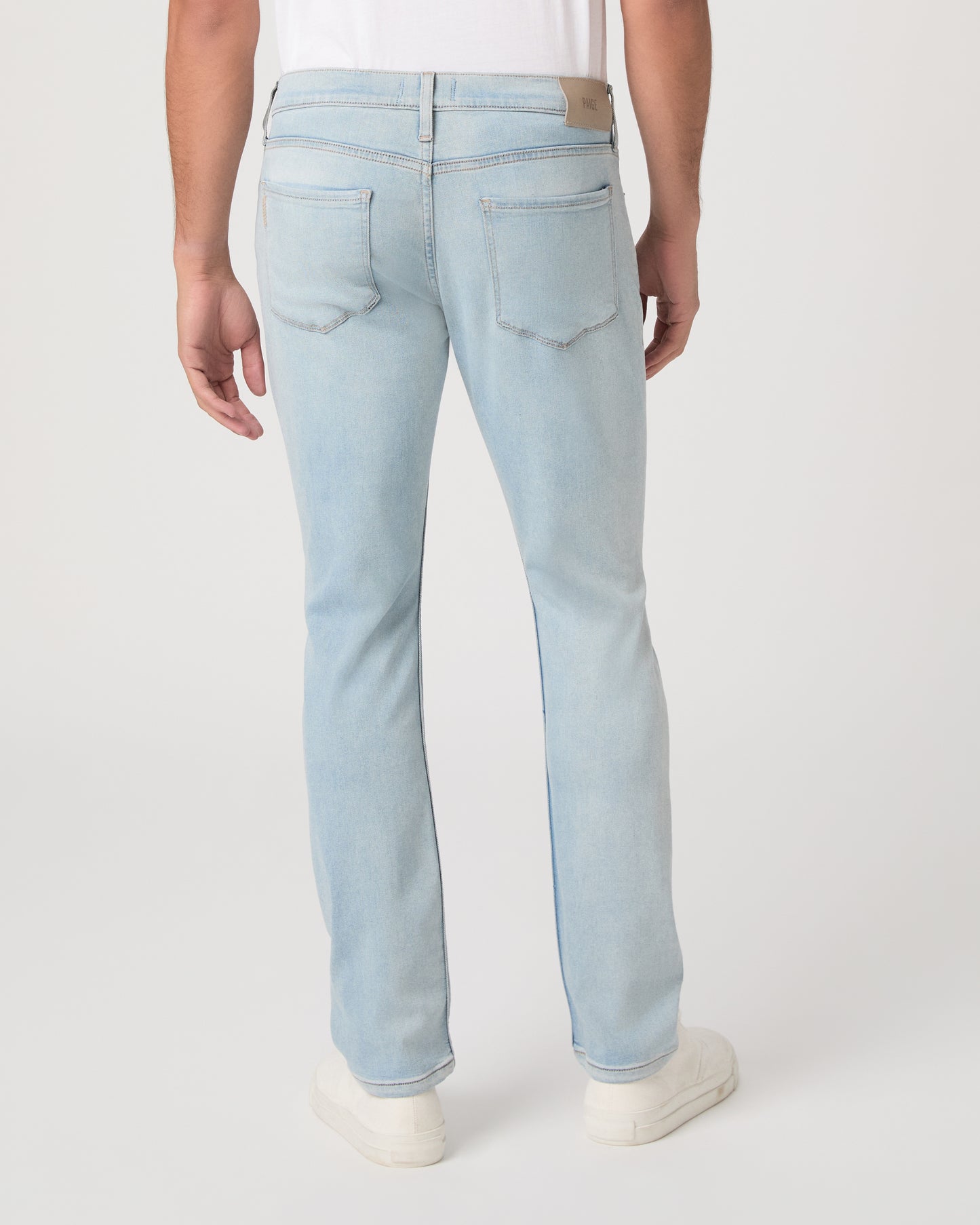 Man wearing a white t-shirt, light blue jeans, and white sneakers on a white background