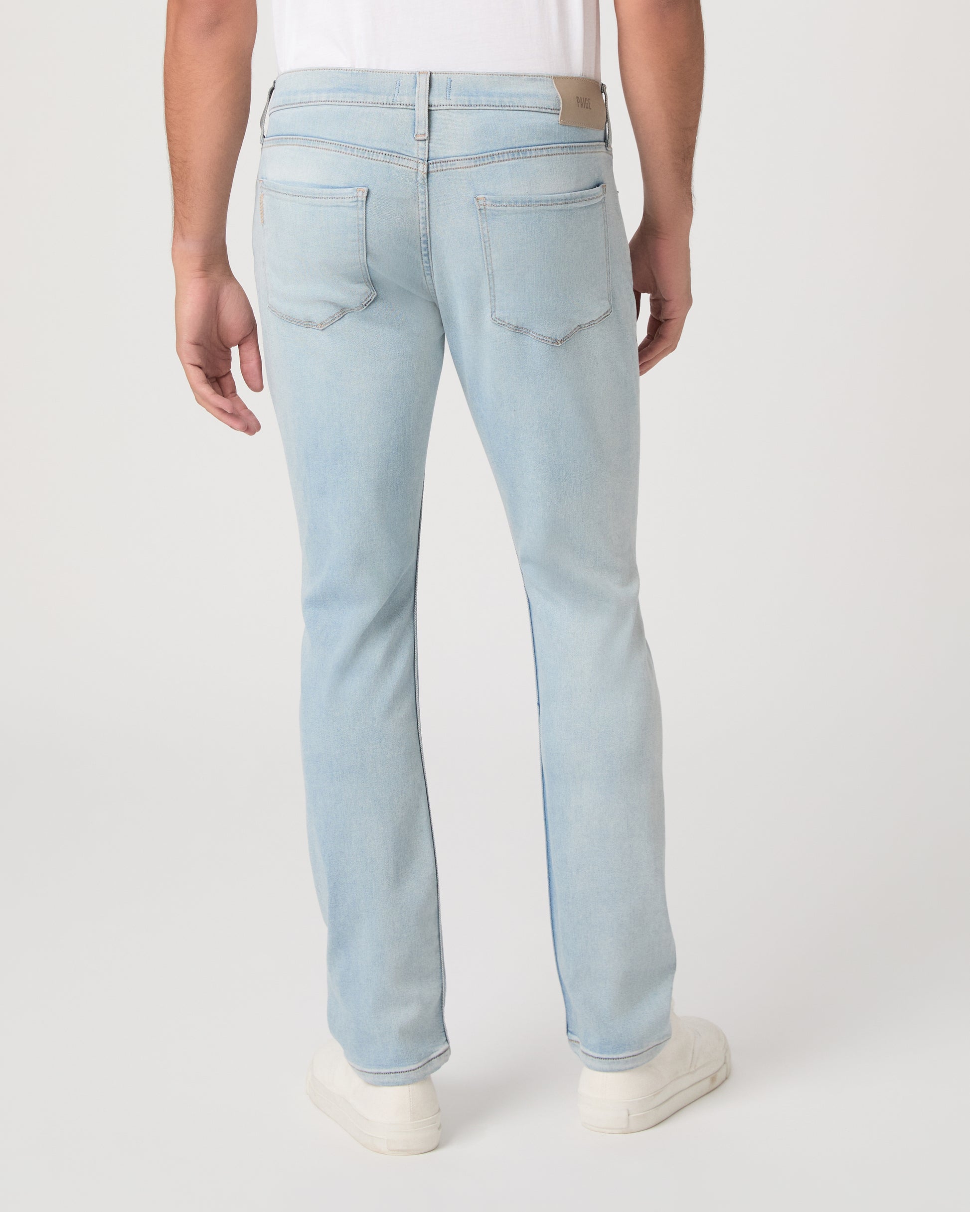 Man wearing a white t-shirt, light blue jeans, and white sneakers on a white background
