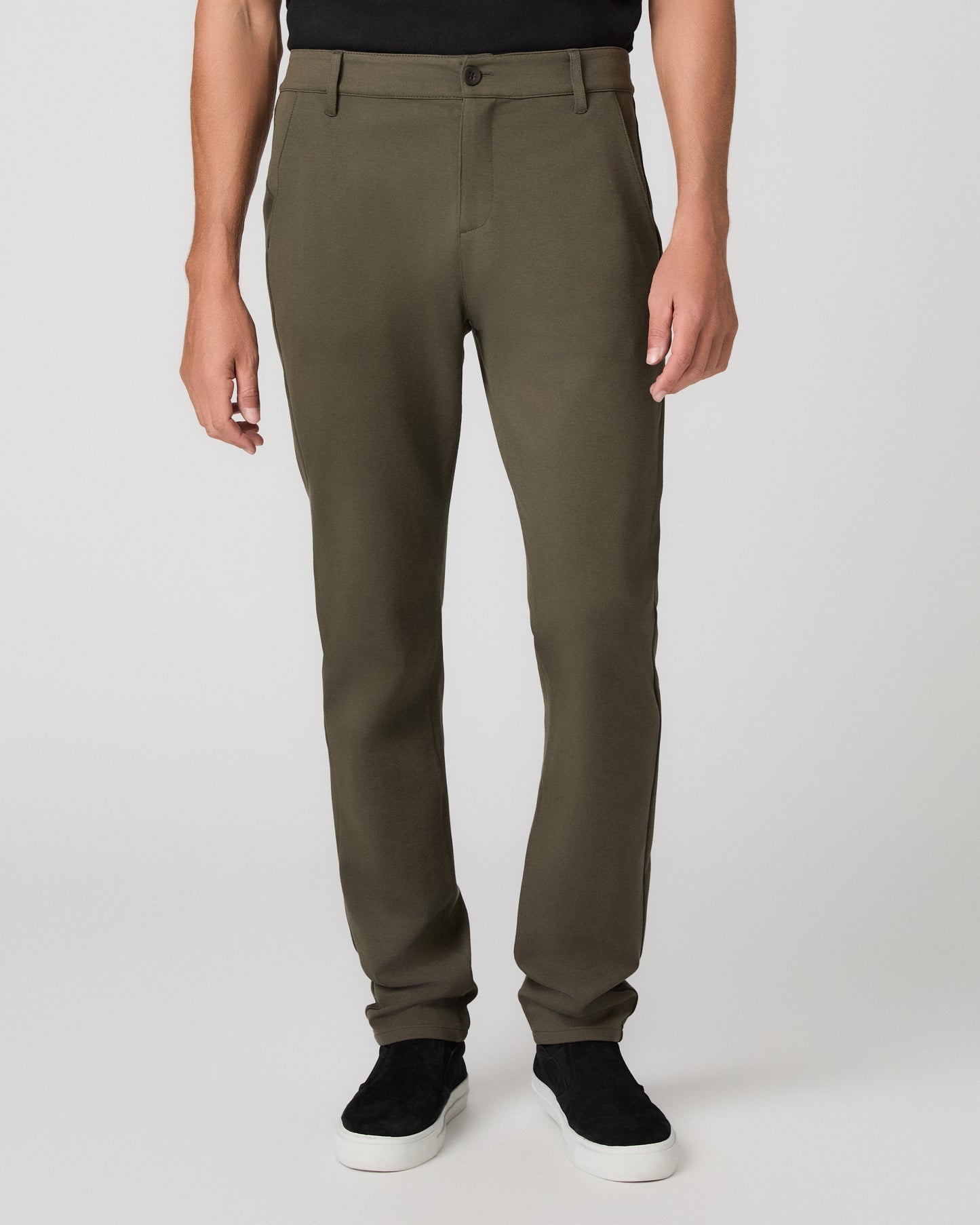 A man modeling a black short-sleeve crewneck t-shirt, olive green pants, and black slip-on shoes against a light gray studio background.