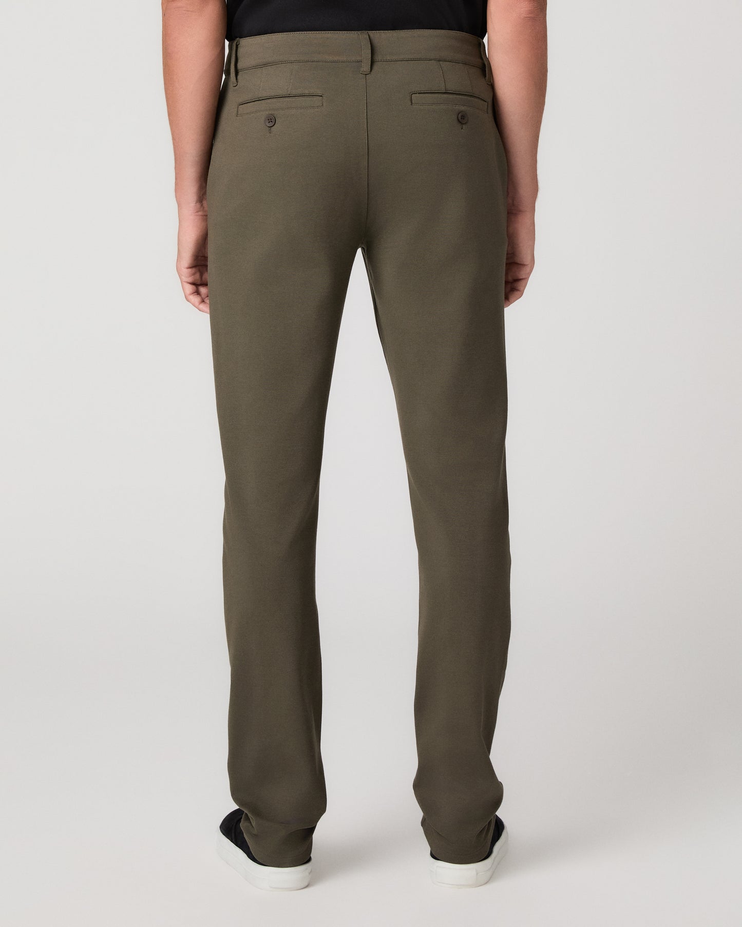 A man modeling a black short-sleeve crewneck t-shirt, olive green pants, and black slip-on shoes against a light gray studio background.