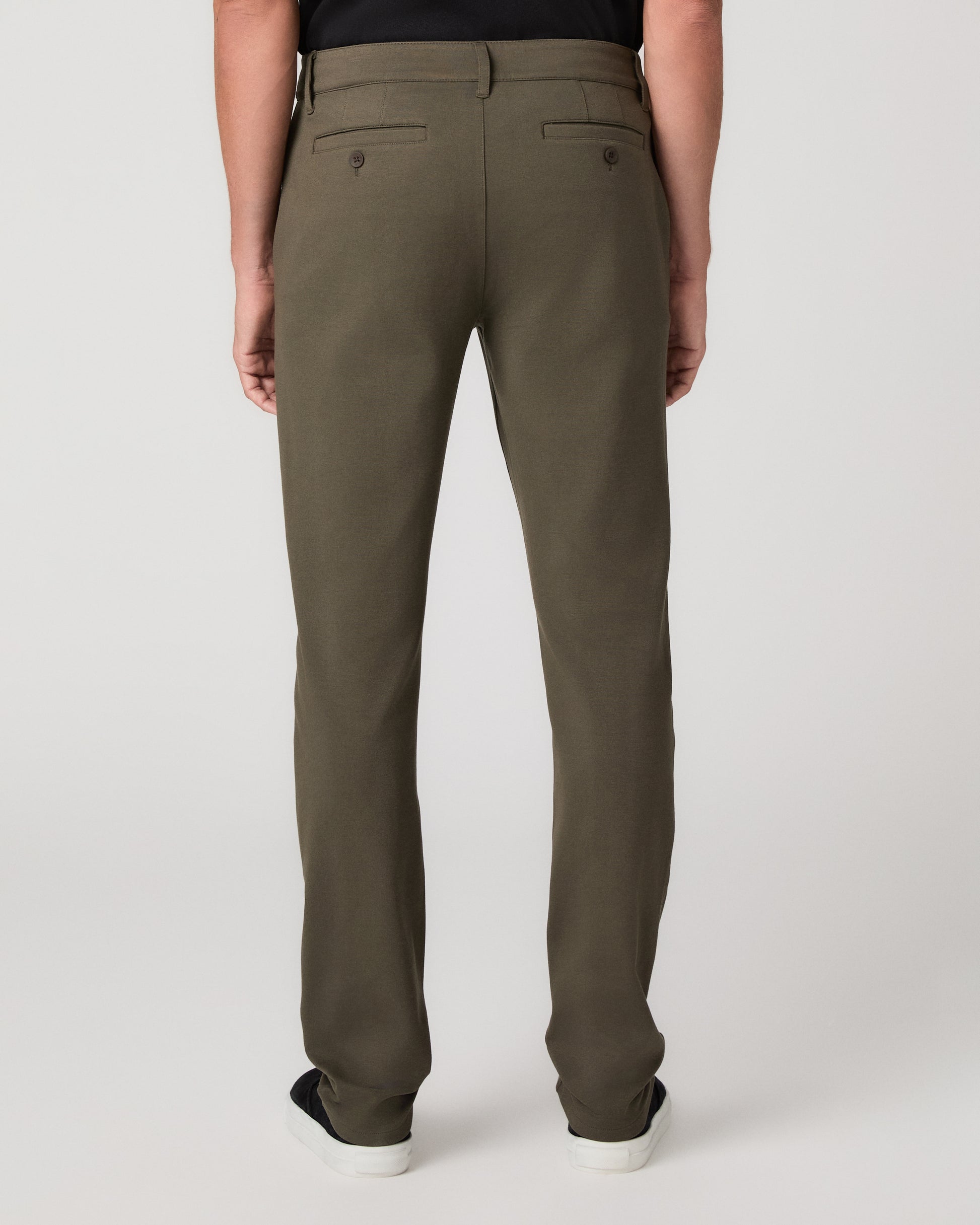 A man modeling a black short-sleeve crewneck t-shirt, olive green pants, and black slip-on shoes against a light gray studio background.