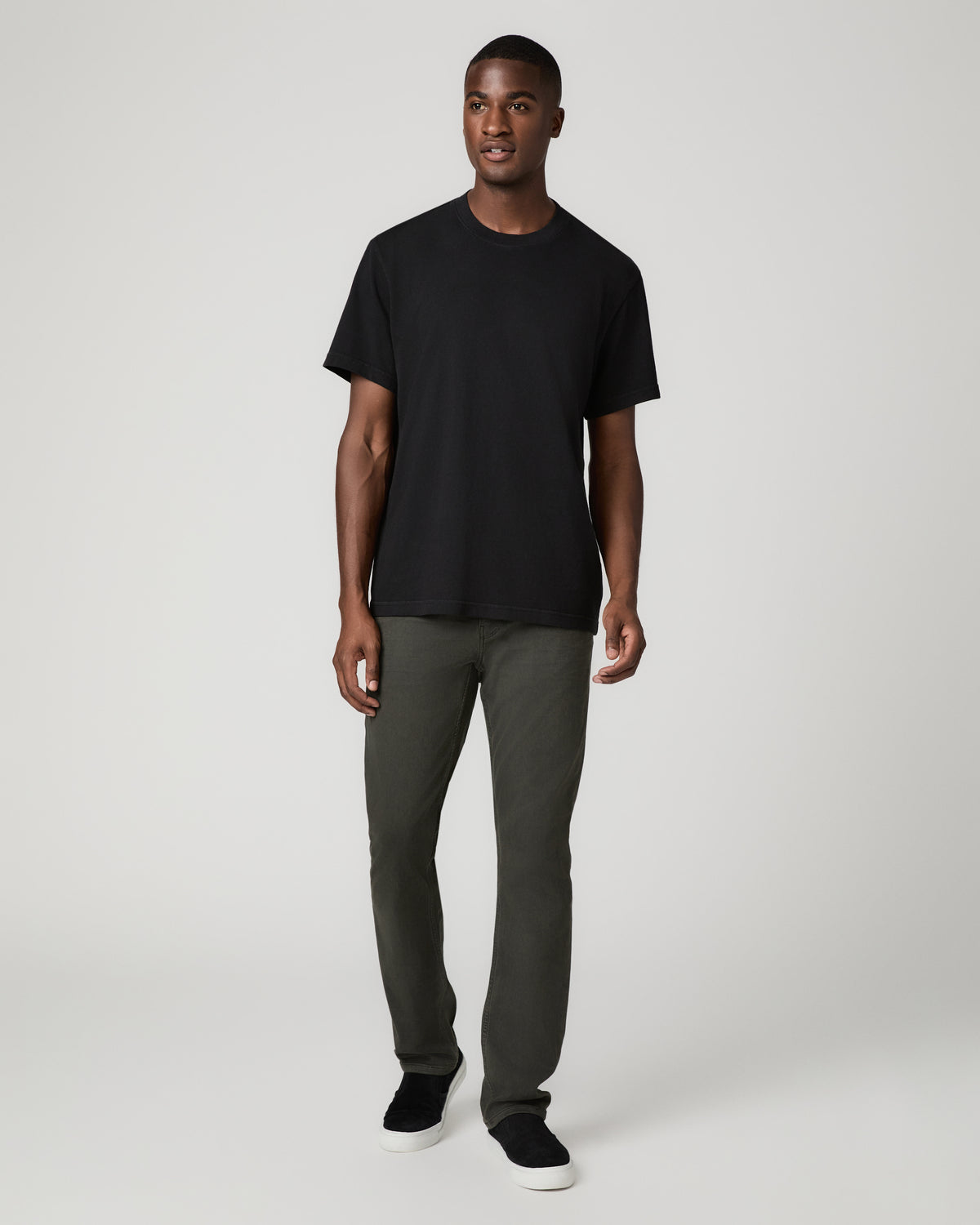 Full-length front view of a man wearing a black crew-neck t-shirt, paired with greenish-black Vintage Deep Woods slim straight jeans and black leather shoes, arms at his sides.