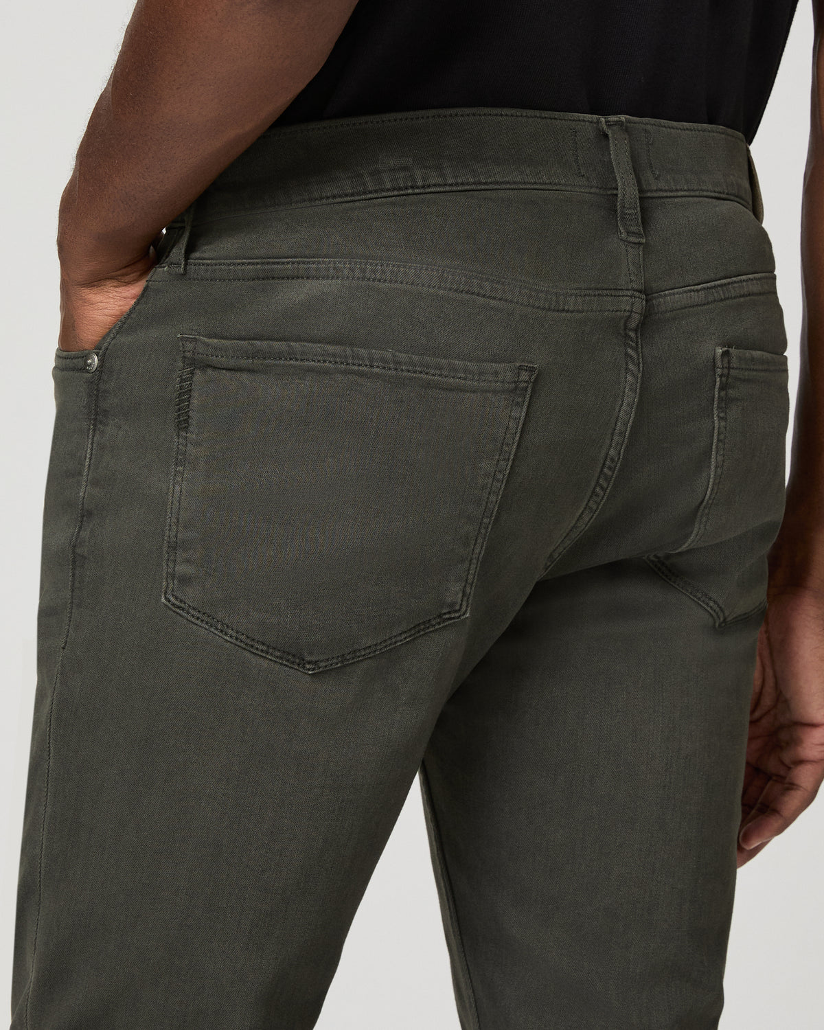 Close-up of the back pocket stitching on the greenish-black denim, hand tucked into the pocket.