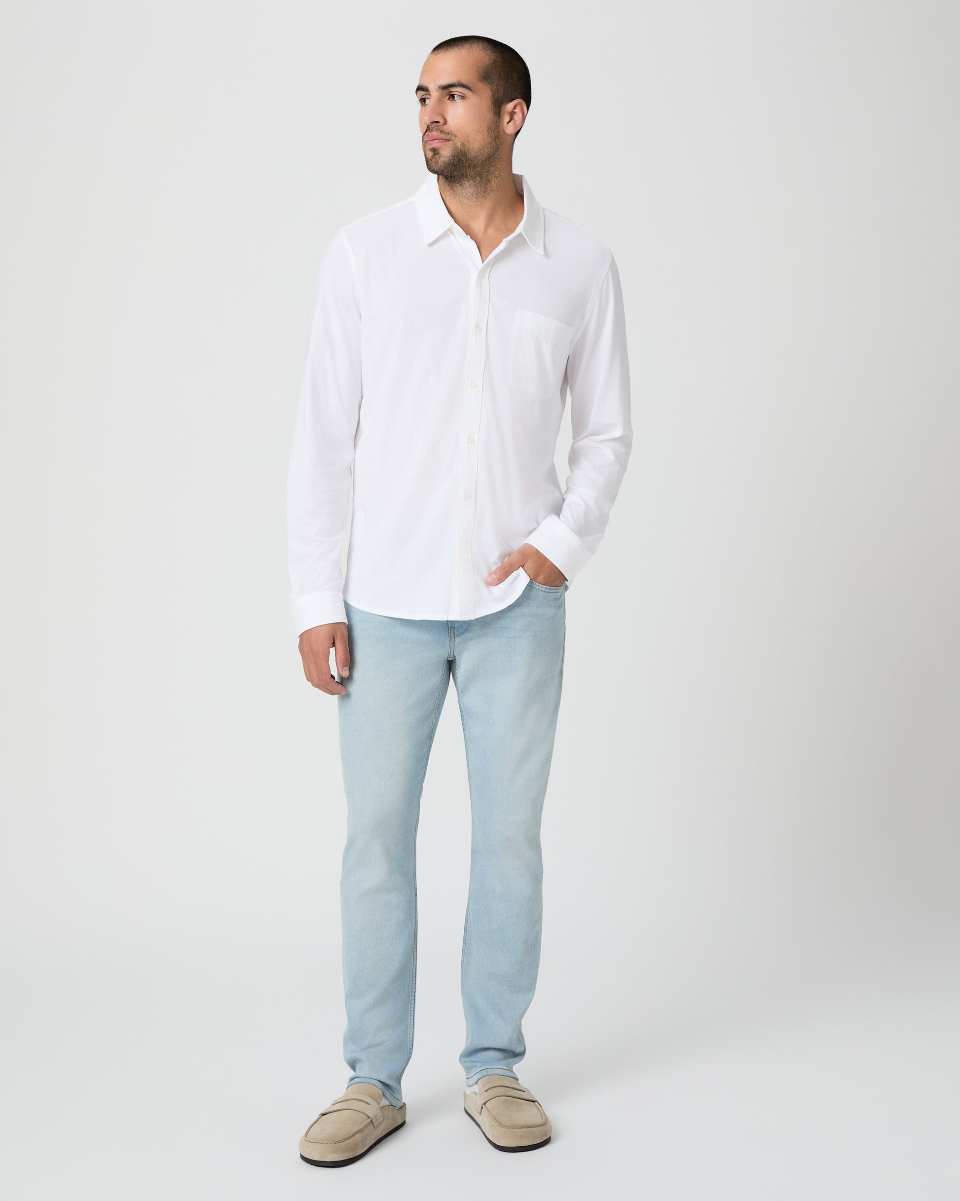 Man wearing a white shirt and light blue jeans against a white background
