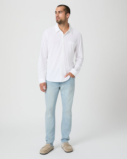 Man wearing a white shirt and light blue jeans against a white background