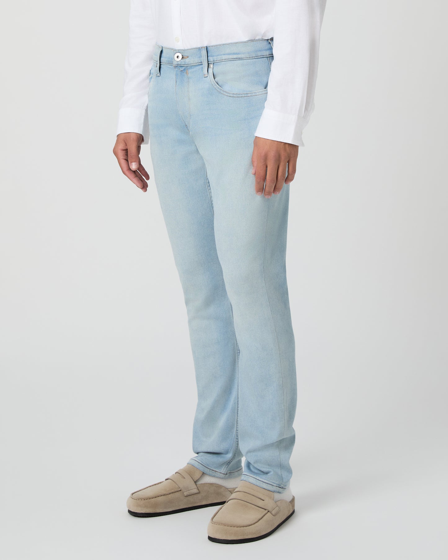 Man wearing a white shirt and light blue jeans against a white background