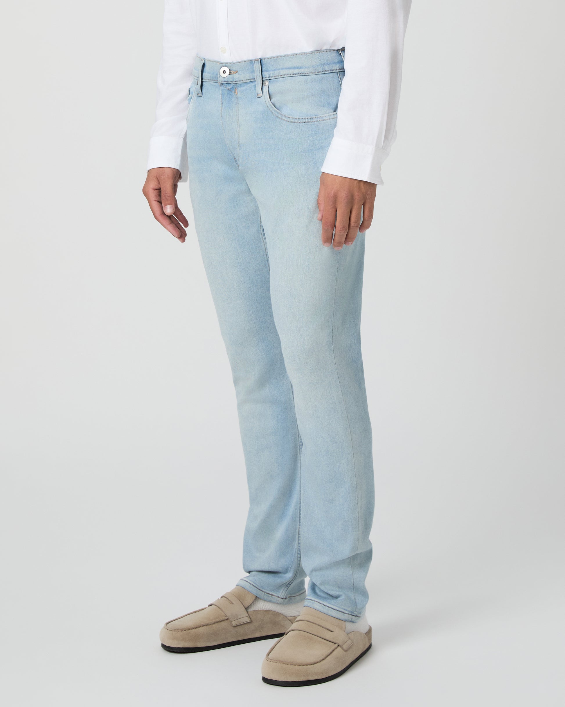 Man wearing a white shirt and light blue jeans against a white background