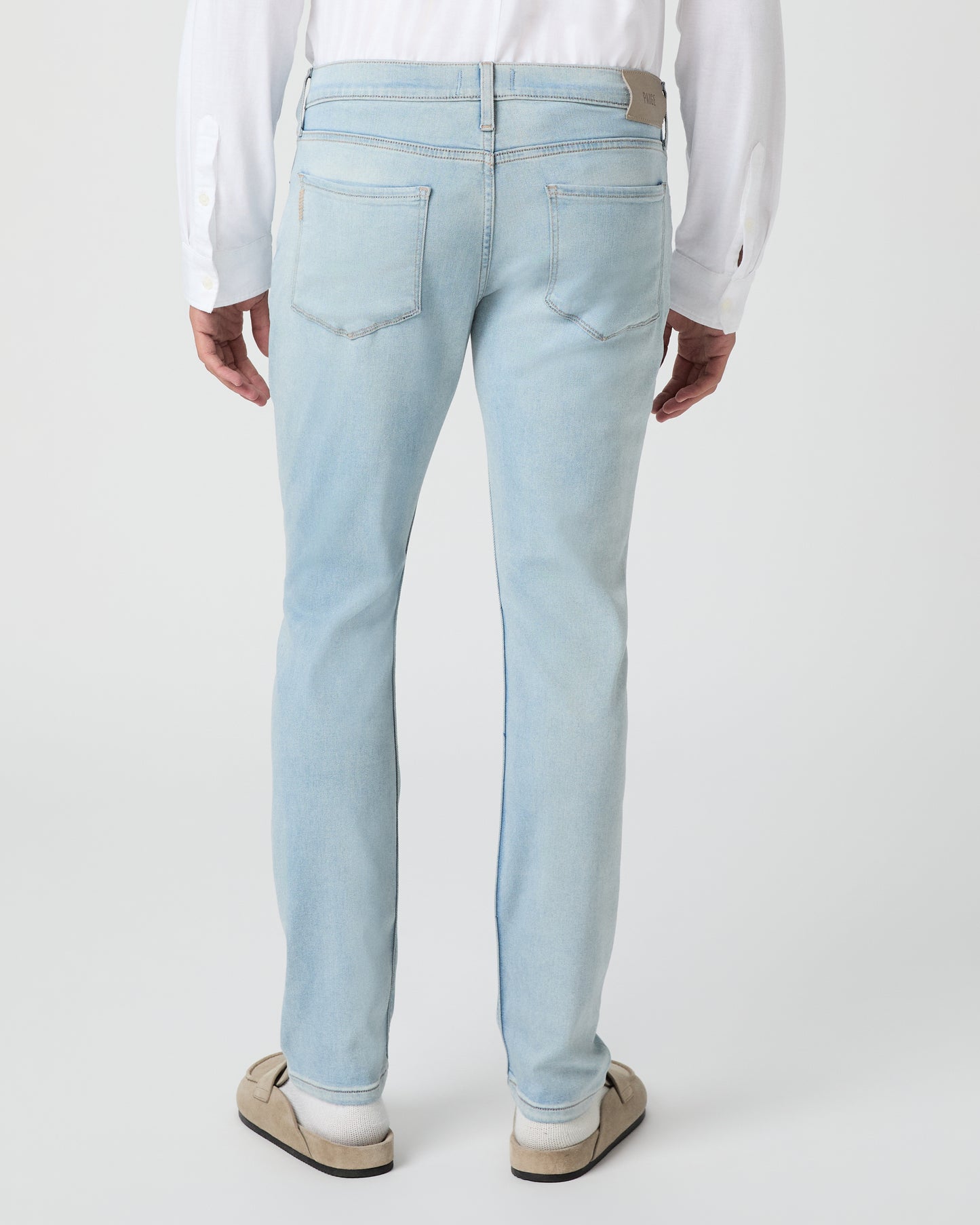 Man wearing a white shirt and light blue jeans against a white background