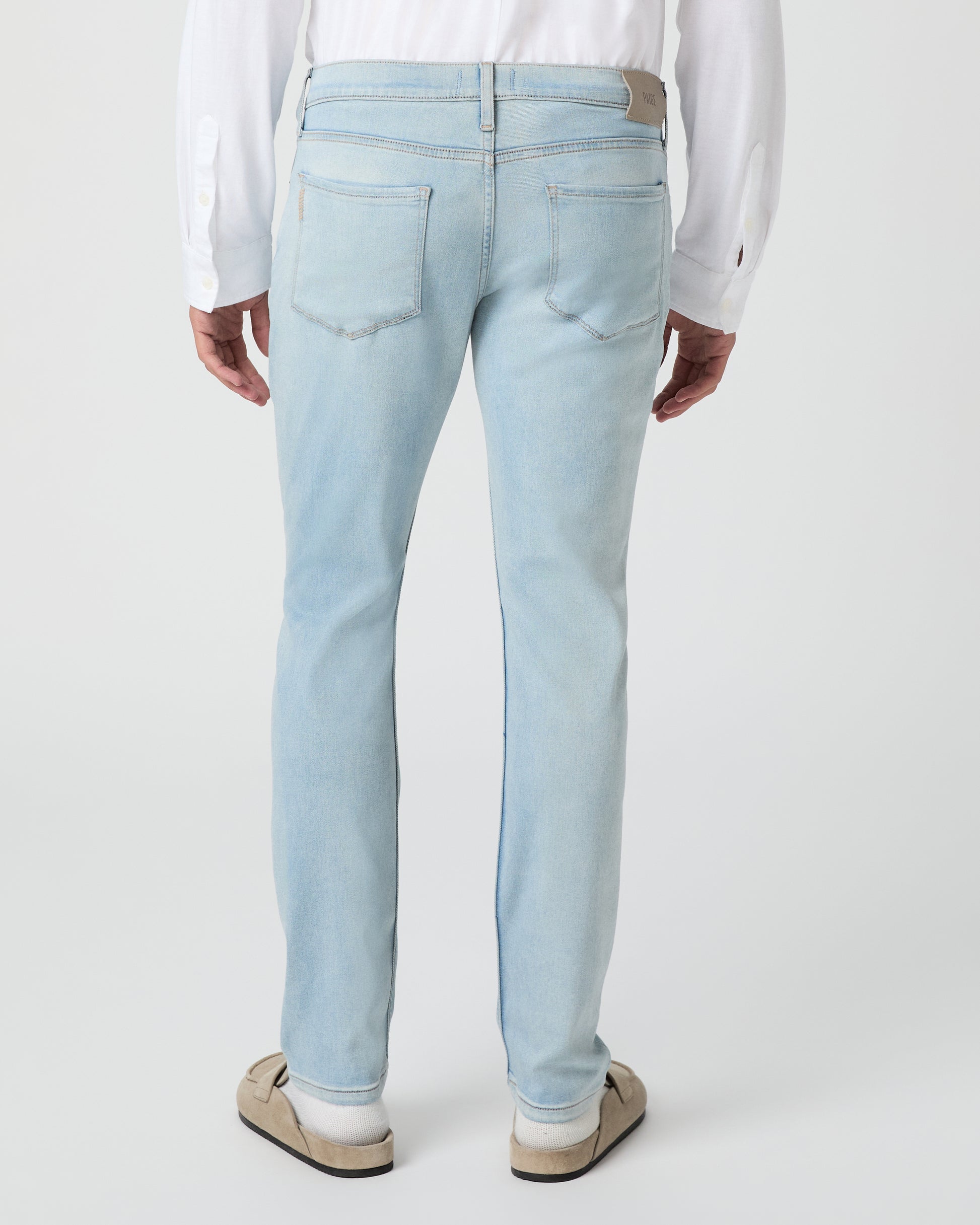 Man wearing a white shirt and light blue jeans against a white background