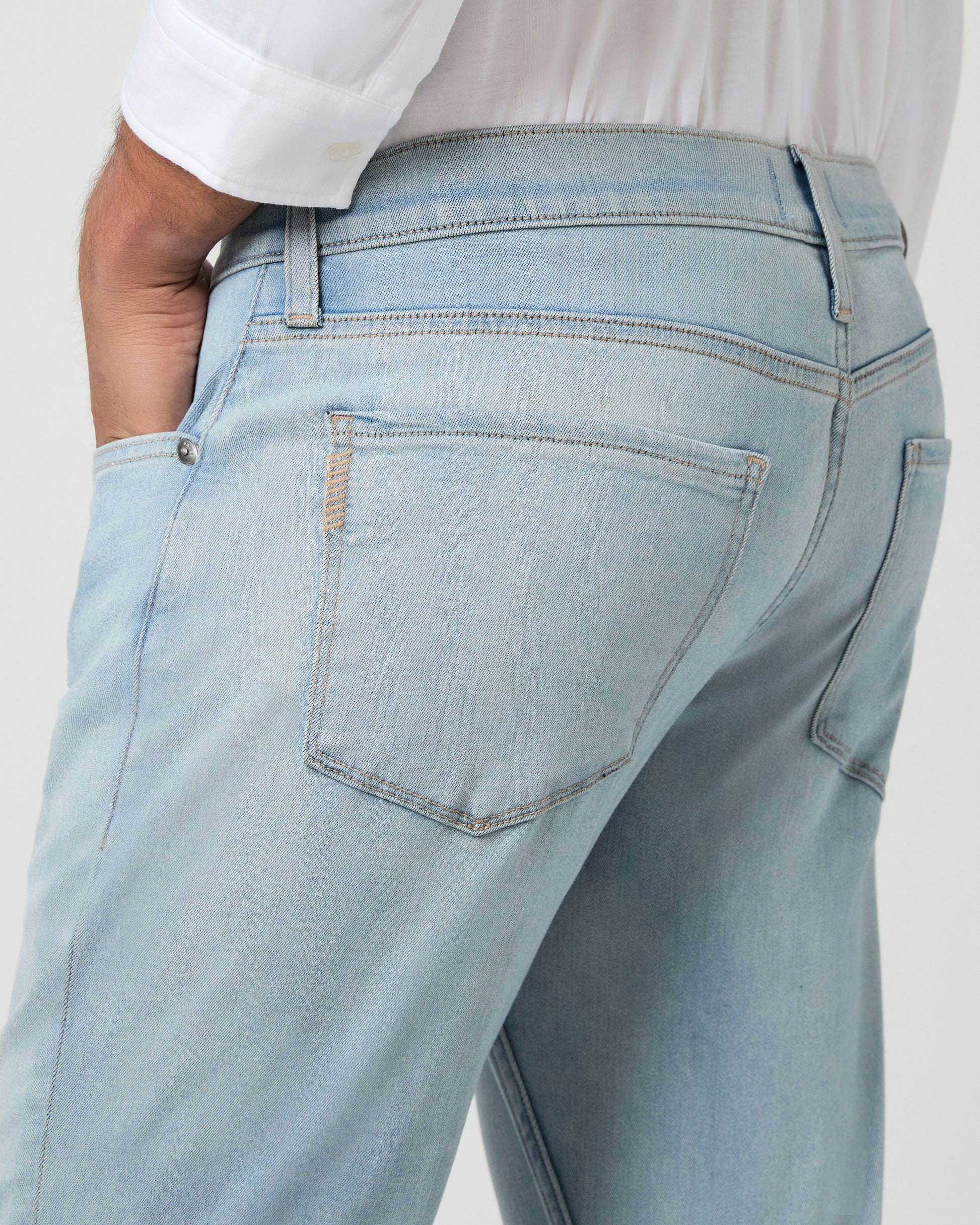 Man wearing a white shirt and light blue jeans against a white background