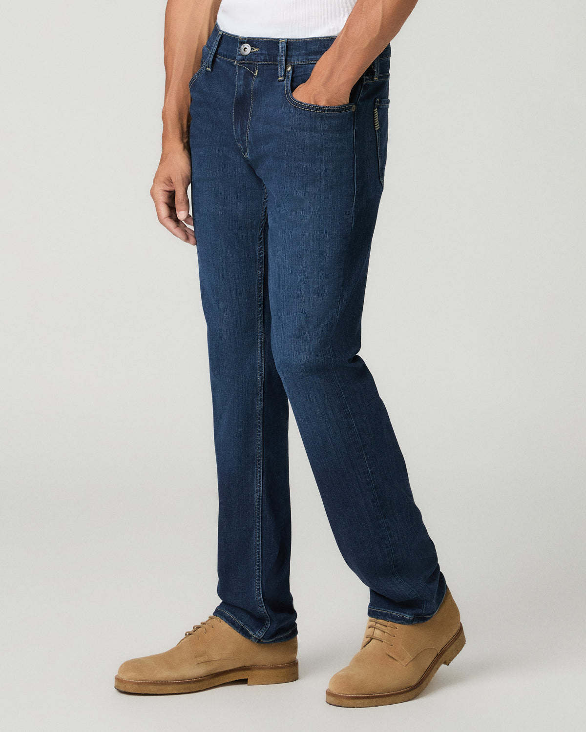 Side profile view from the waist down of a man wearing deep blue slim-straight jeans, paired with tan suede shoes.