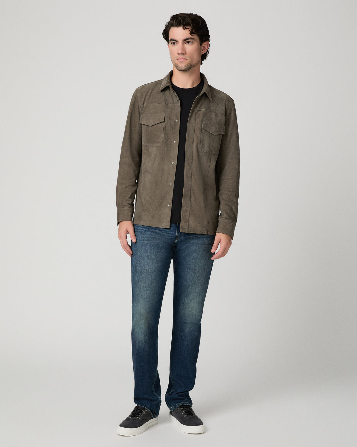 Man wearing grey jacket and black shirt with dark jeans against a white background