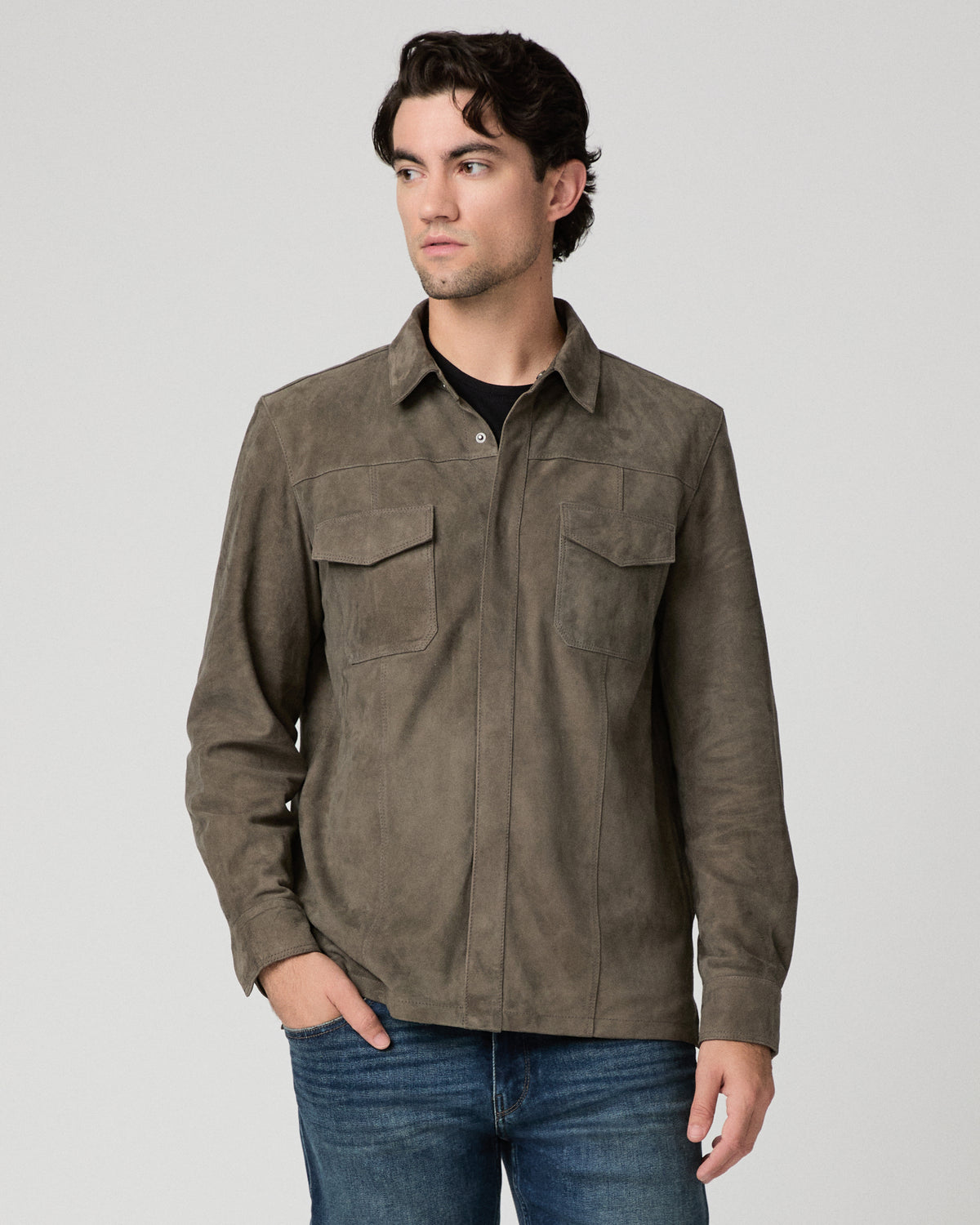 Man wearing grey jacket and black shirt with dark jeans against a white background