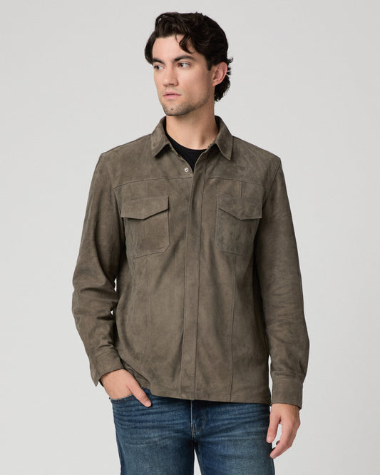 Man wearing grey jacket and black shirt with dark jeans against a white background