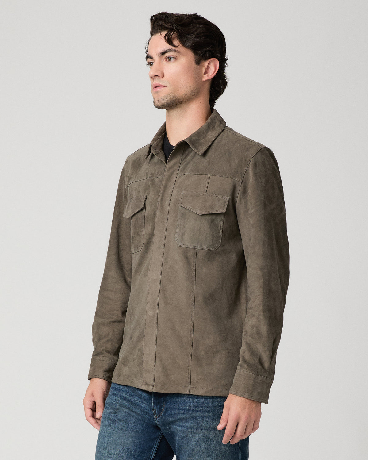 Man wearing grey jacket and black shirt with dark jeans against a white background
