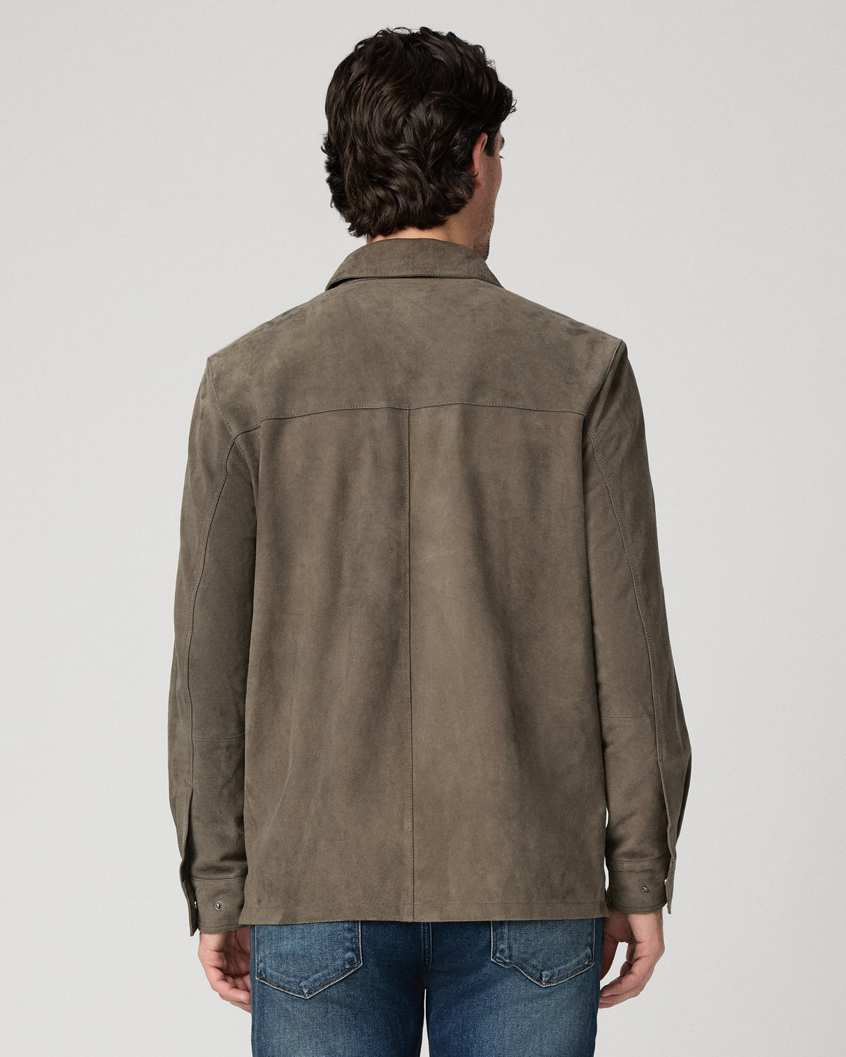 Man wearing grey jacket and black shirt with dark jeans against a white background