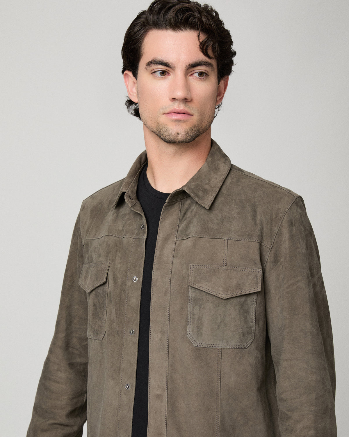 Man wearing grey jacket and black shirt with dark jeans against a white background