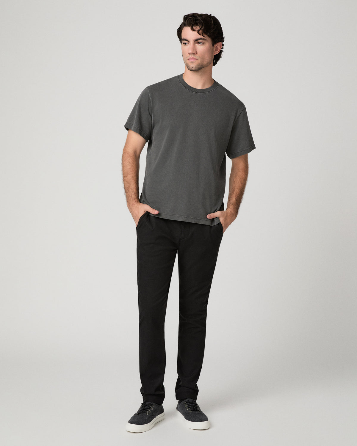 Man wearing grey shirt and black pants against a white background