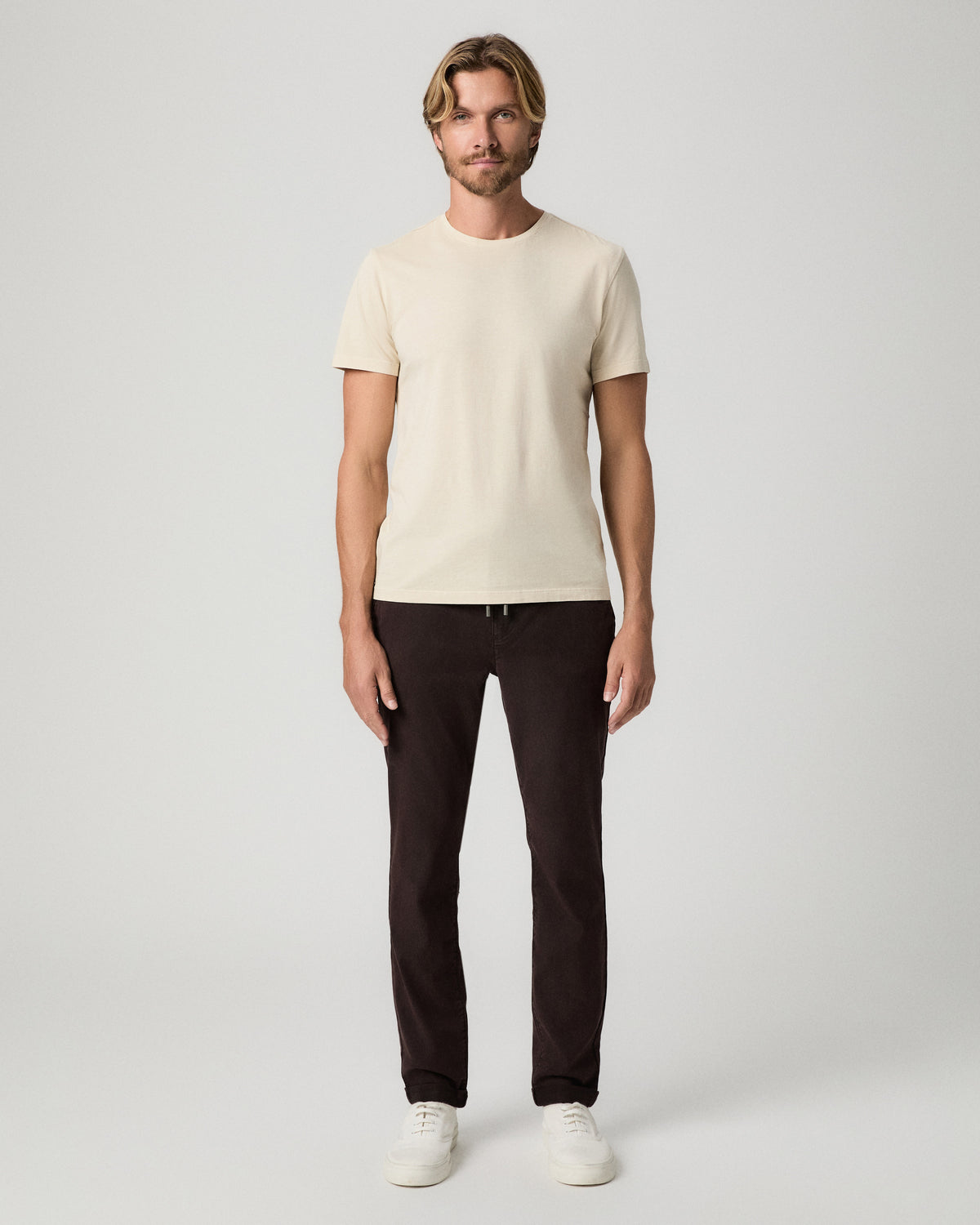 Full-length view of model standing with arms at his sides, wearing a cream tee with the Fraser Pant in Mole and white sneakers