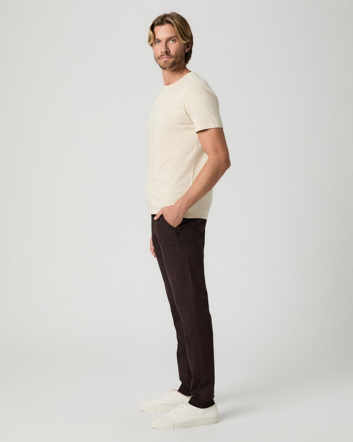 Side profile of model with one hand in his pocket, wearing a cream tee with the Fraser Pant in Mole and white sneakers