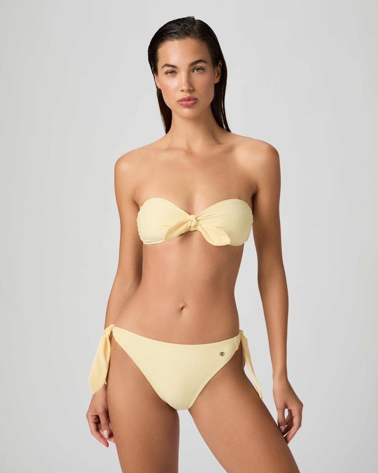 Woman wearing a yellow bikini set against a textured white wall.
