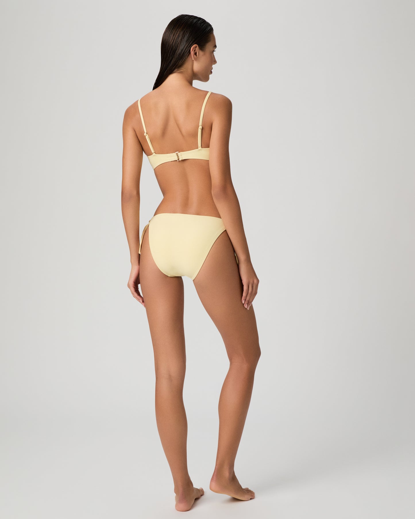 Woman wearing a yellow bikini set against a textured white wall.