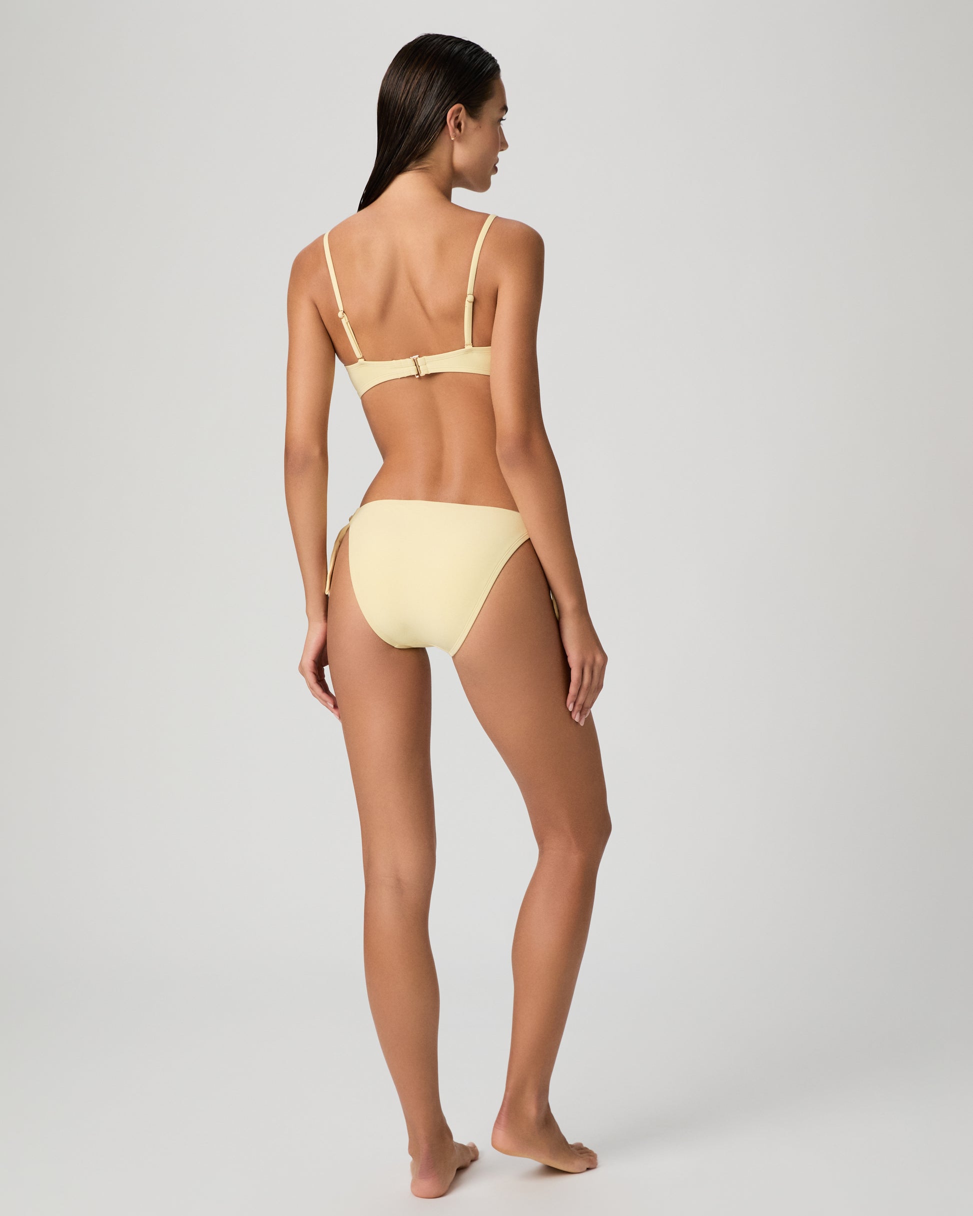 Woman wearing a yellow bikini set against a textured white wall.