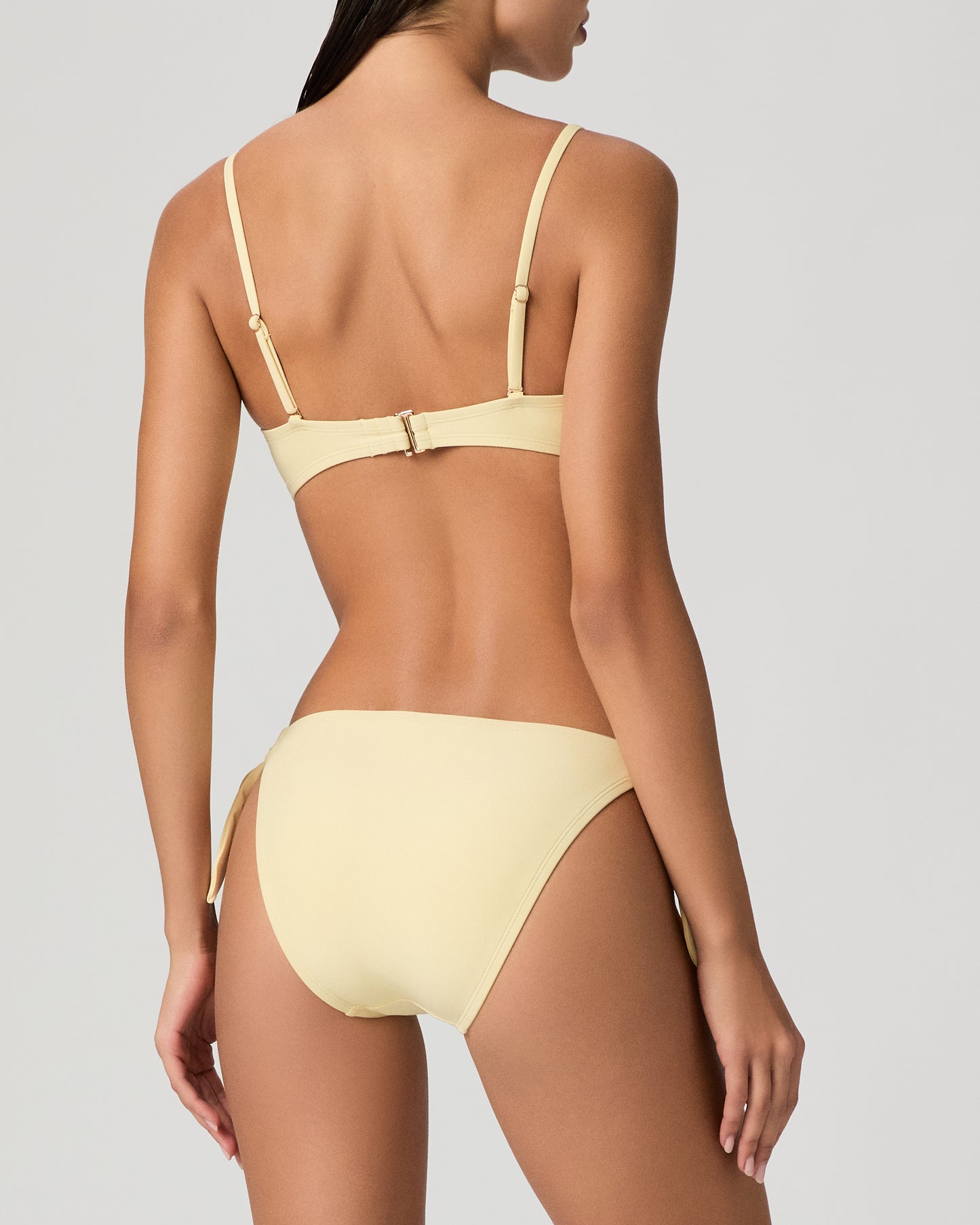 Woman wearing a yellow bikini set against a textured white wall.