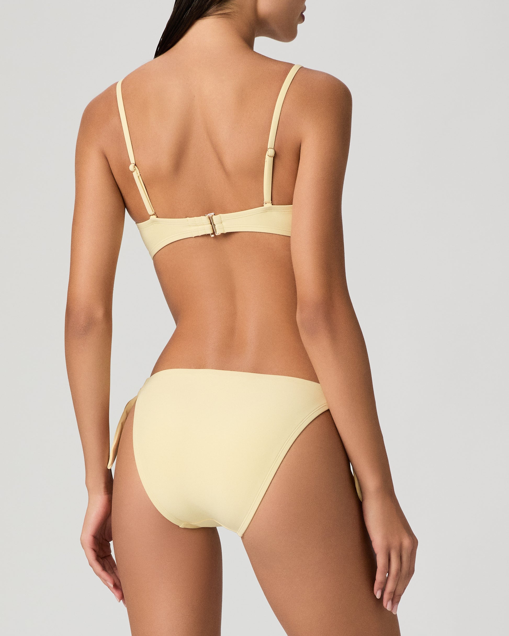 Woman wearing a yellow bikini set against a textured white wall.