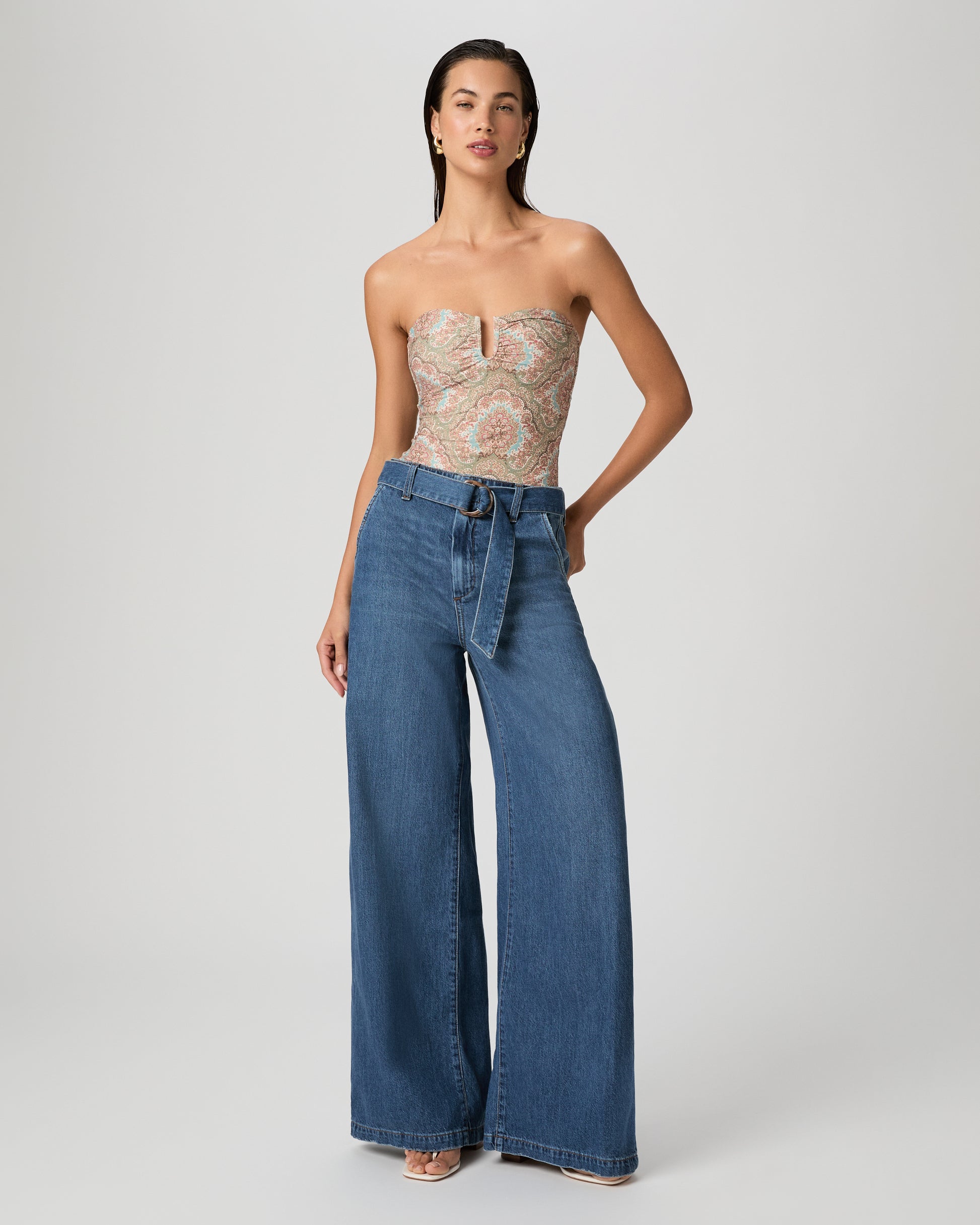 Woman wearing a patterned one-piece swimsuit paired with medium wash jeans on a white background