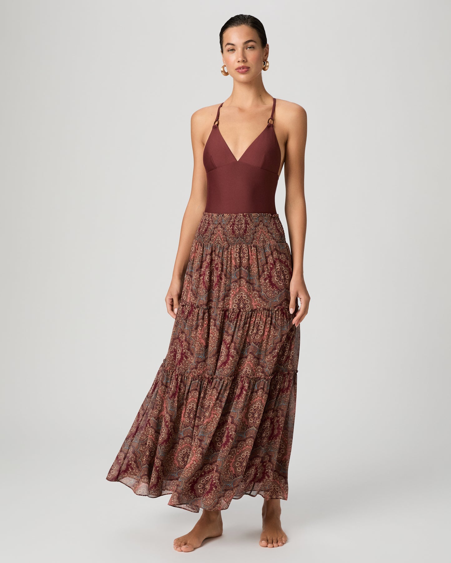 Woman wearing a burgundy one-piece swimsuit paired with a printed midi skirt on a white background