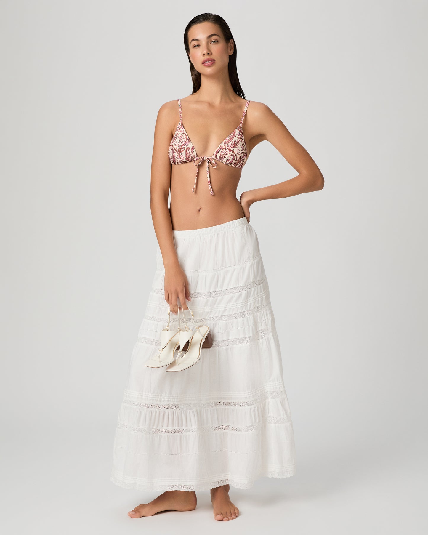 Woman wearing a pink bikini top and white skirt on a plain background