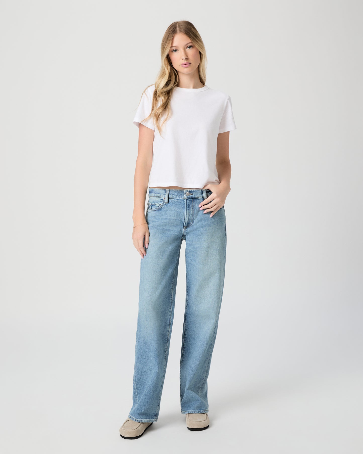 Women wearing white tee and denim paired with beige slipper on a light gray background