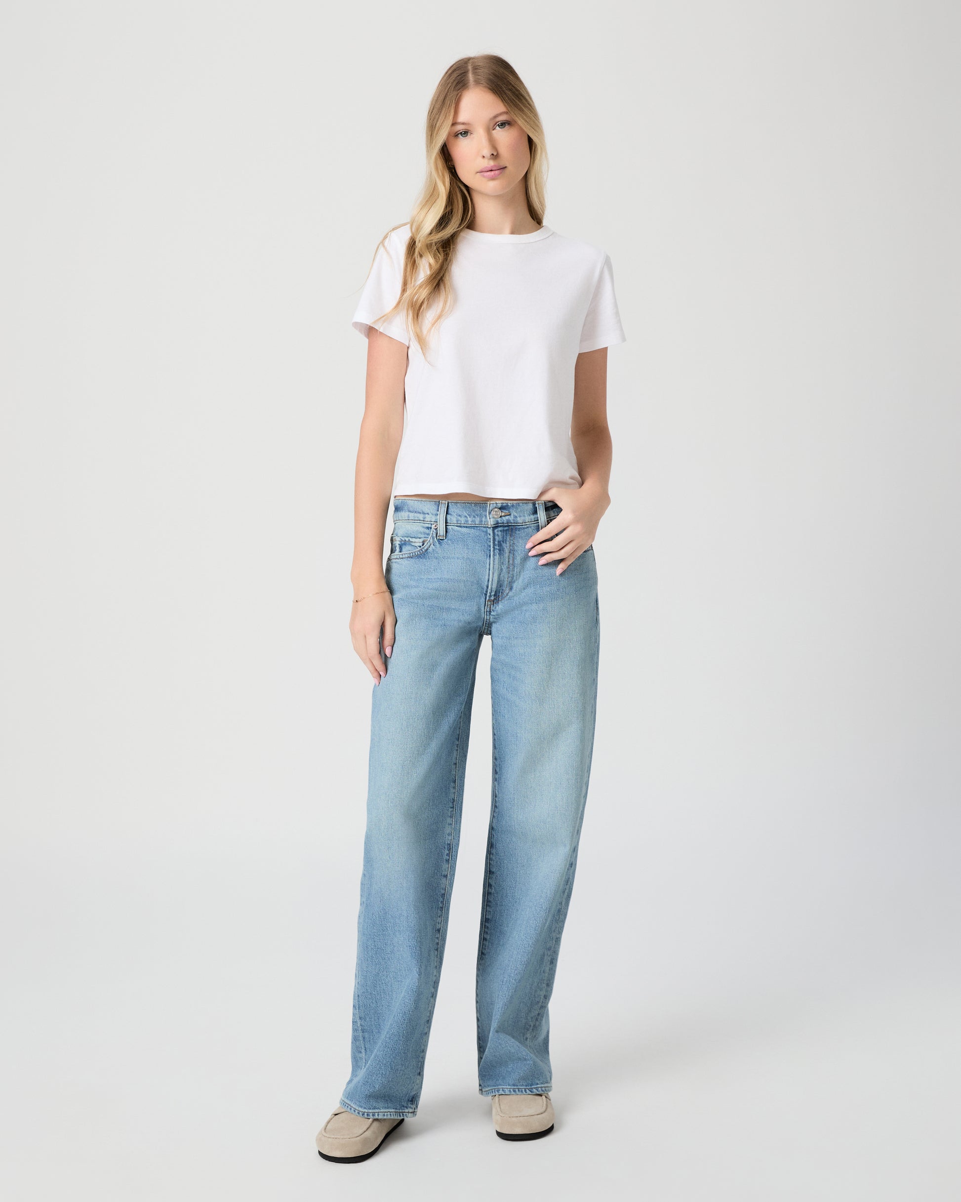 Women wearing white tee and denim paired with beige slipper on a light gray background